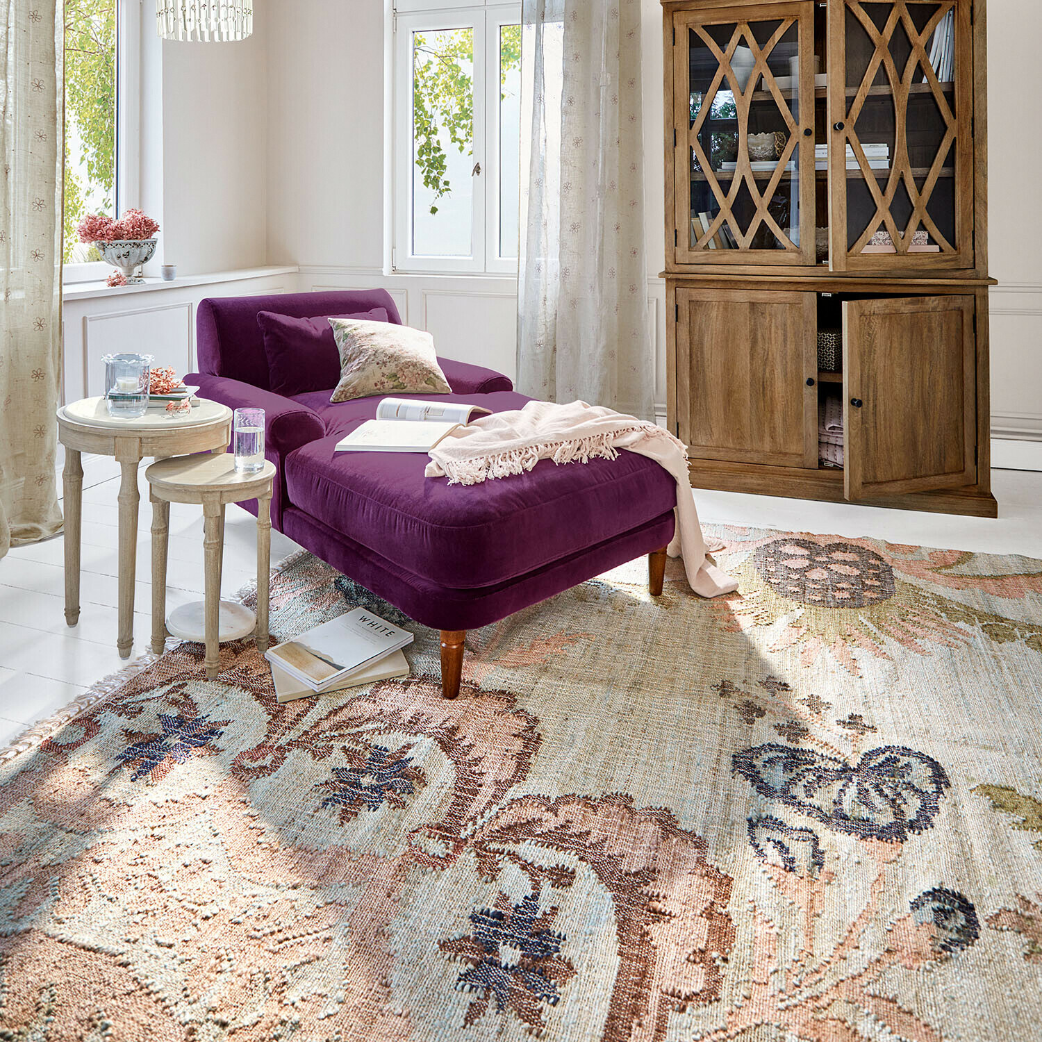 Chaise longue en velours violet dans un salon lumineux avec buffet en bois et tapis décoratif