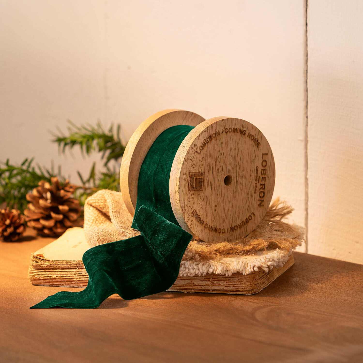 Ruban de velours Phaedra Bobine en bois avec ruban en velours vert sur fond rustique avec pommes de pin et livre ancien