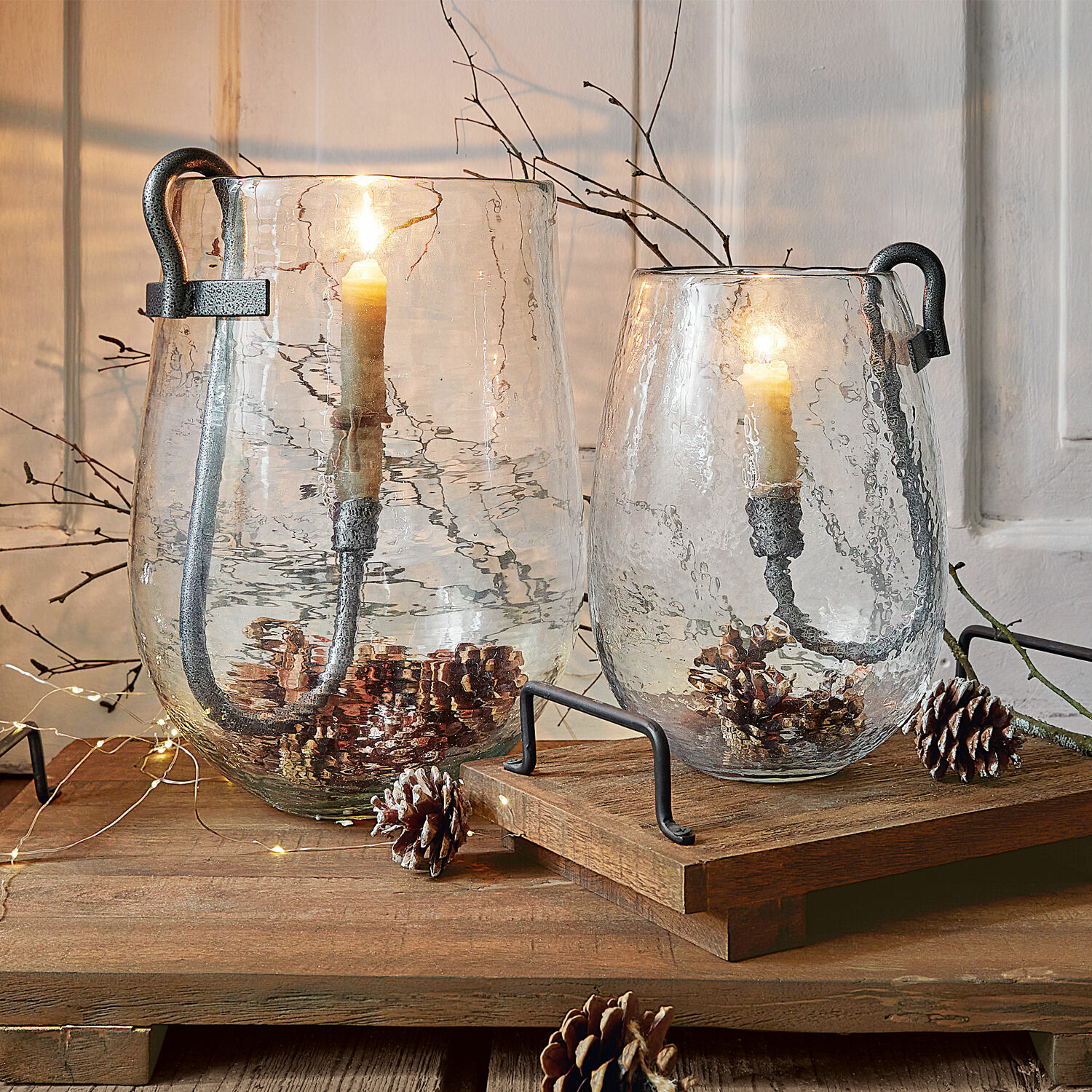 Deux lanternes en verre transparent avec poignées en métal et bougies, décorées de pommes de pin