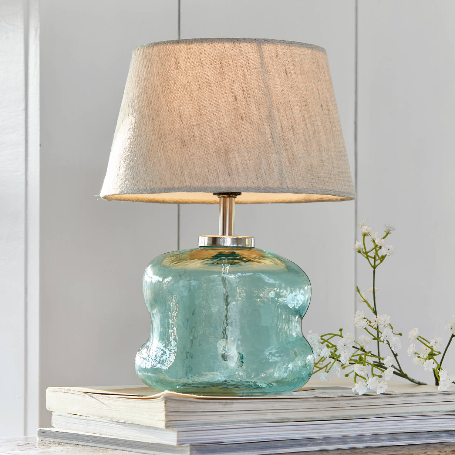 Lampe de table en verre bleu avec abat-jour beige posée sur des livres, décoration intérieure