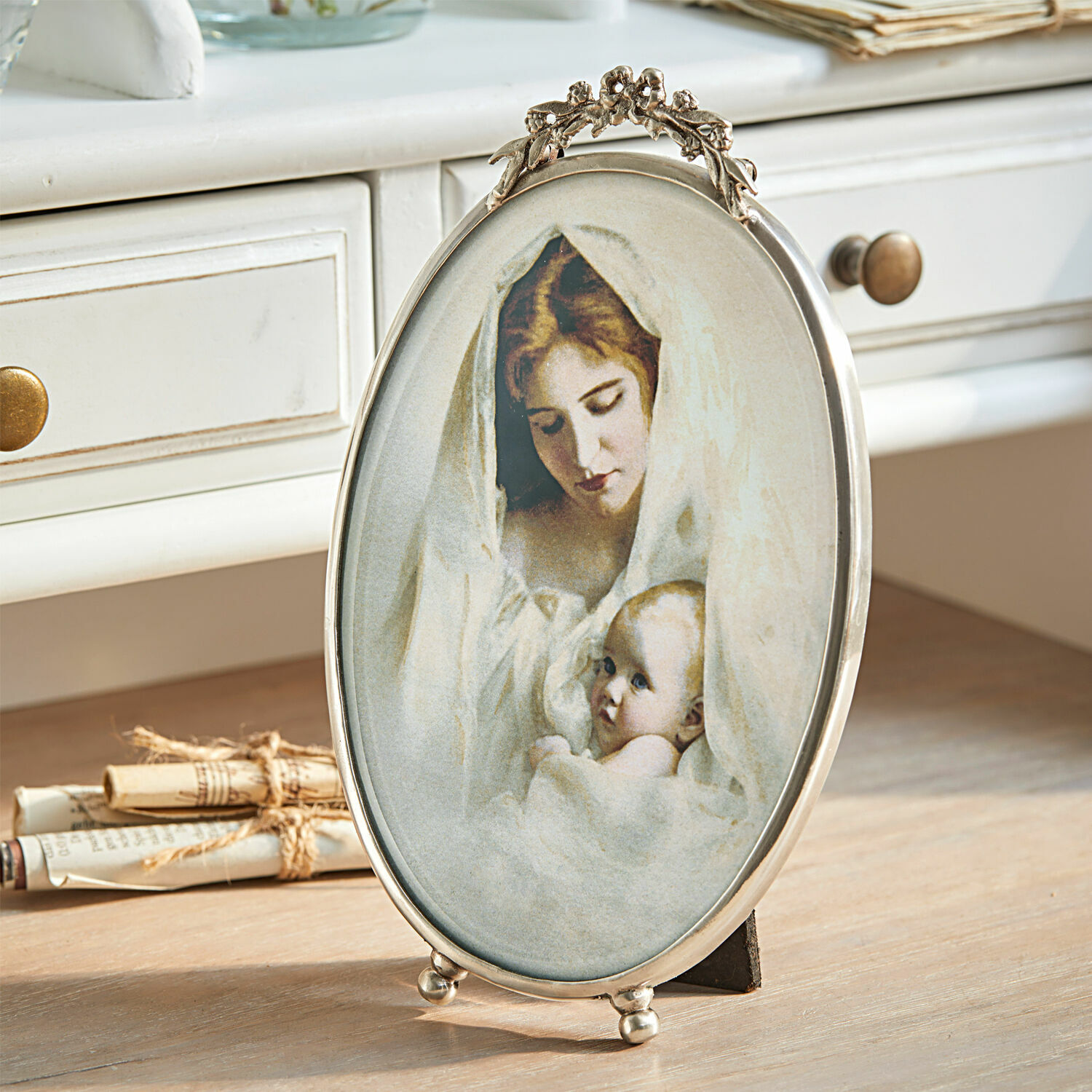 Cadre-photo Grange Cadre ovale en métal avec image d'une mère et son bébé enveloppés de tissus blancs sur une table en bois