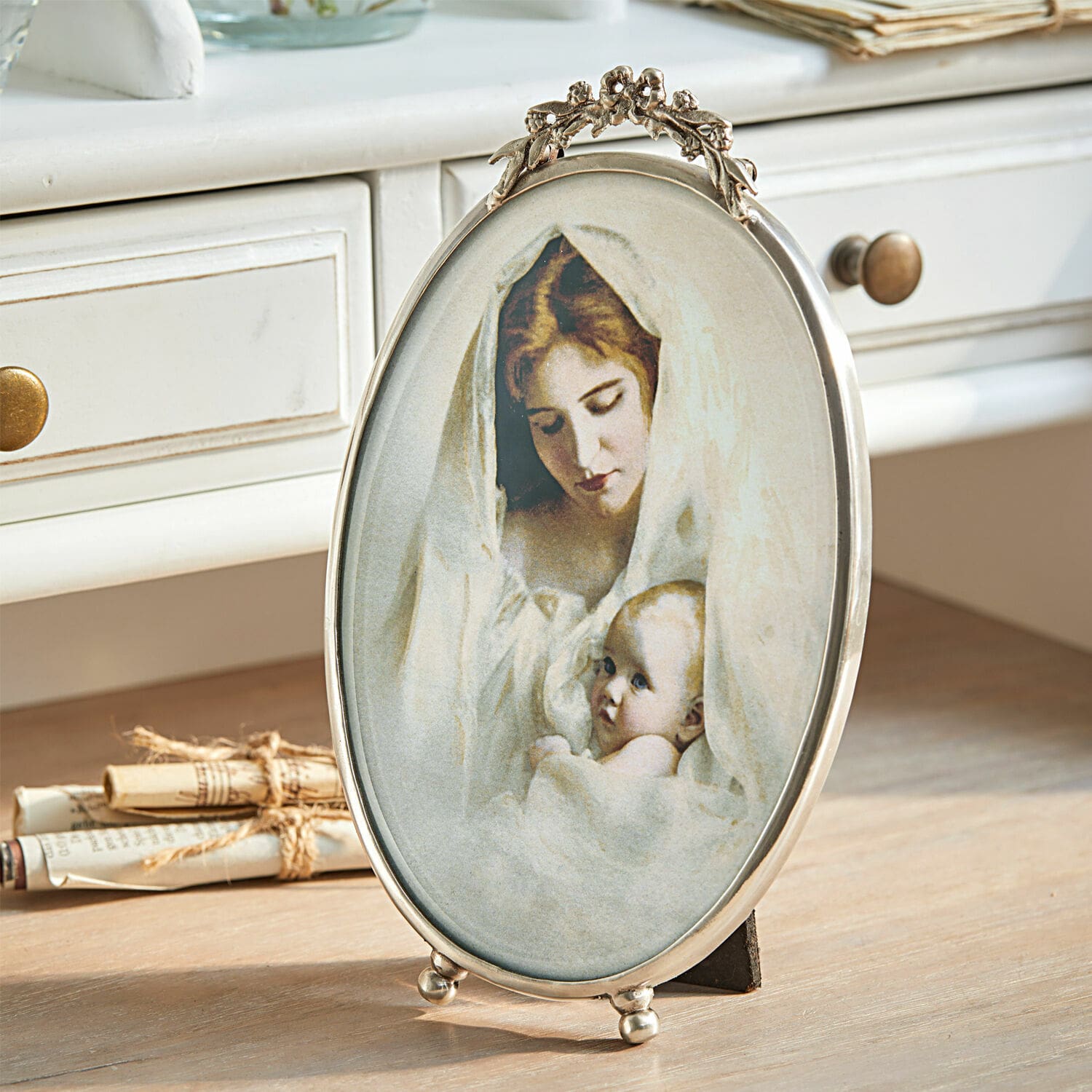 Cadre-photo Grange Cadre ovale en métal avec image d'une mère et son bébé enveloppés de tissus blancs sur une table en bois