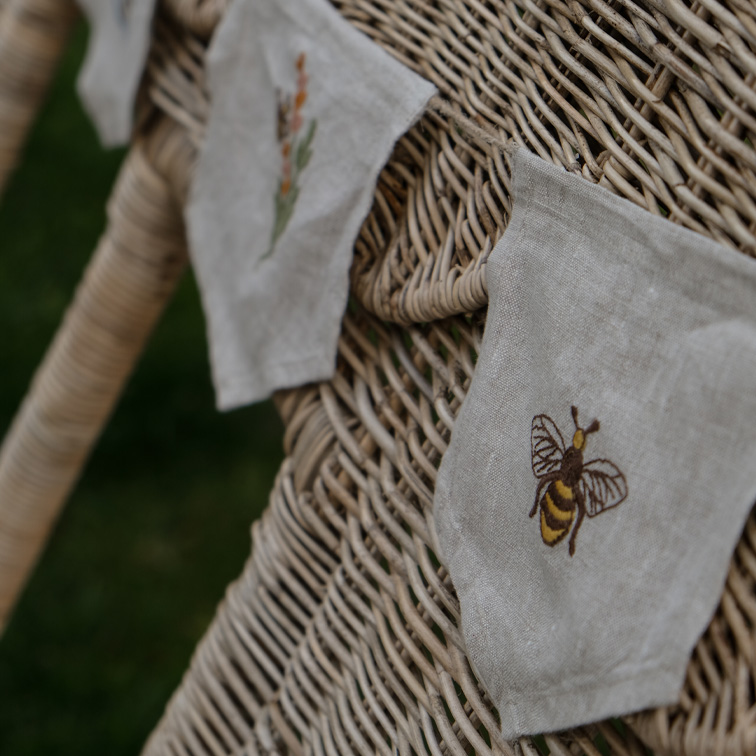 Petits sacs décoratifs en lin avec broderies d'abeille et de fleurs sur chaise en osier beige
