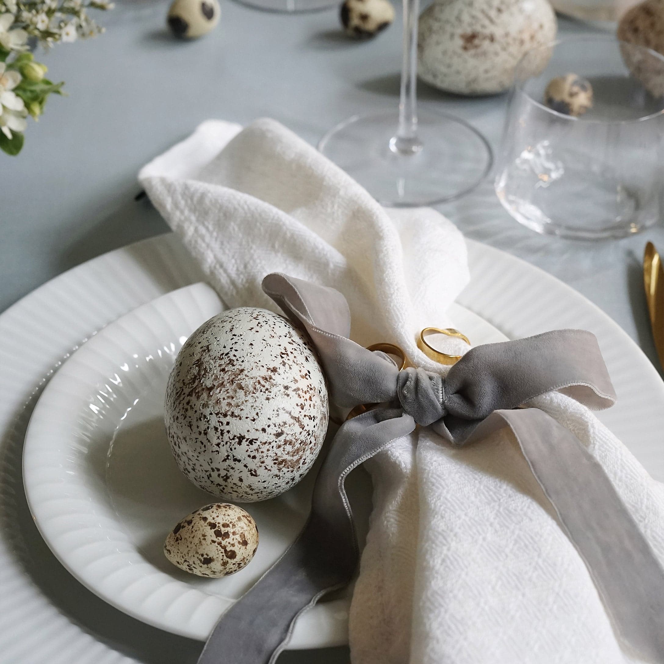 Assiettes blanches avec œufs tachetés décoratifs et serviette en lin nouée d'un ruban gris sur table