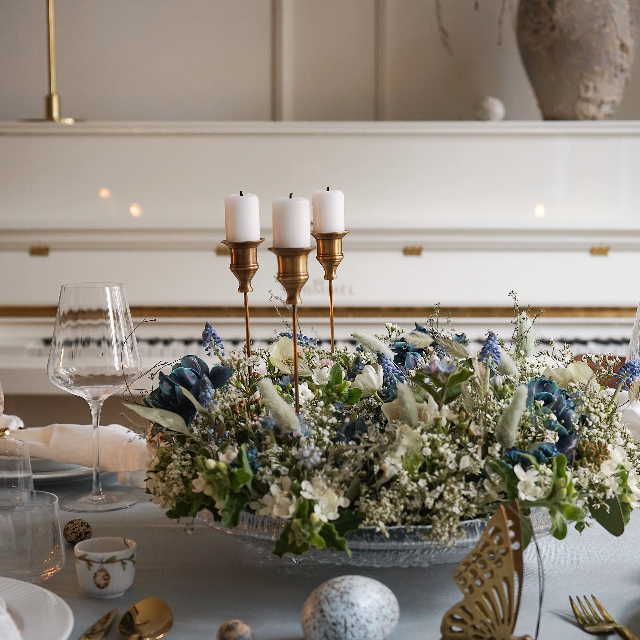 Bougeoir décoratif avec trois bougies blanches et arrangement floral sur base en verre