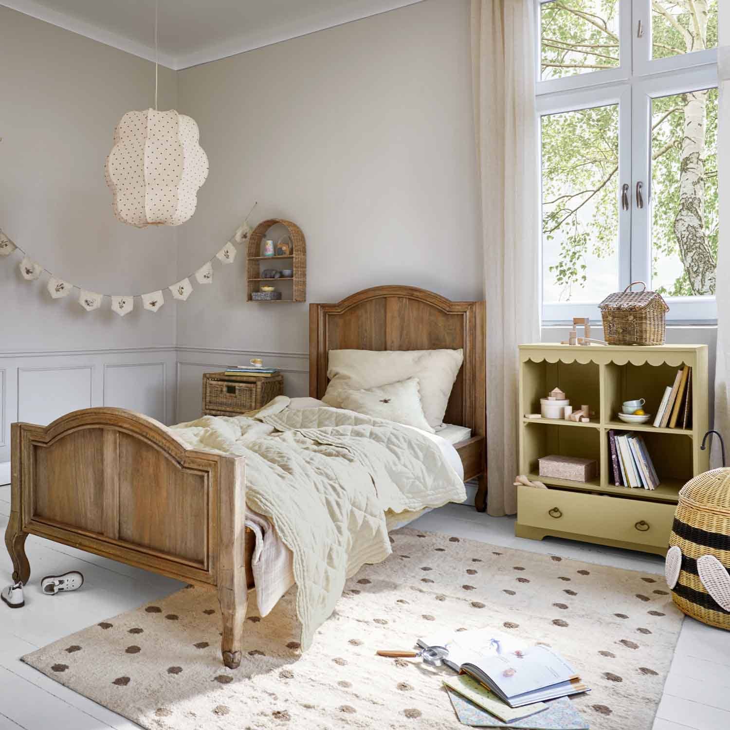 Lit enfant en bois naturel avec couette beige et petite armoire pastel pour jouets dans une chambre lumineuse