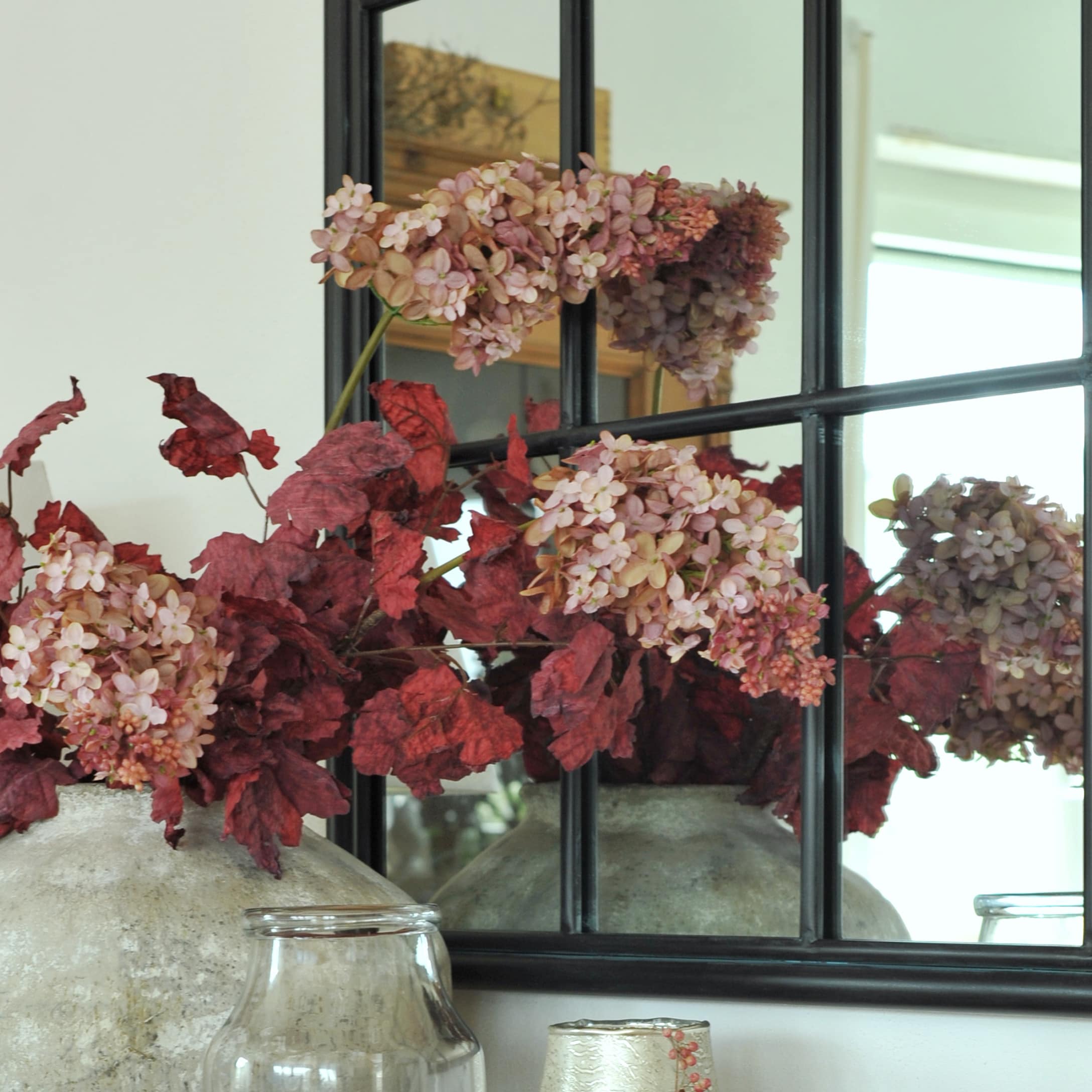 Vase décoratif avec feuilles rouges et fleurs roses devant un miroir au style vintage