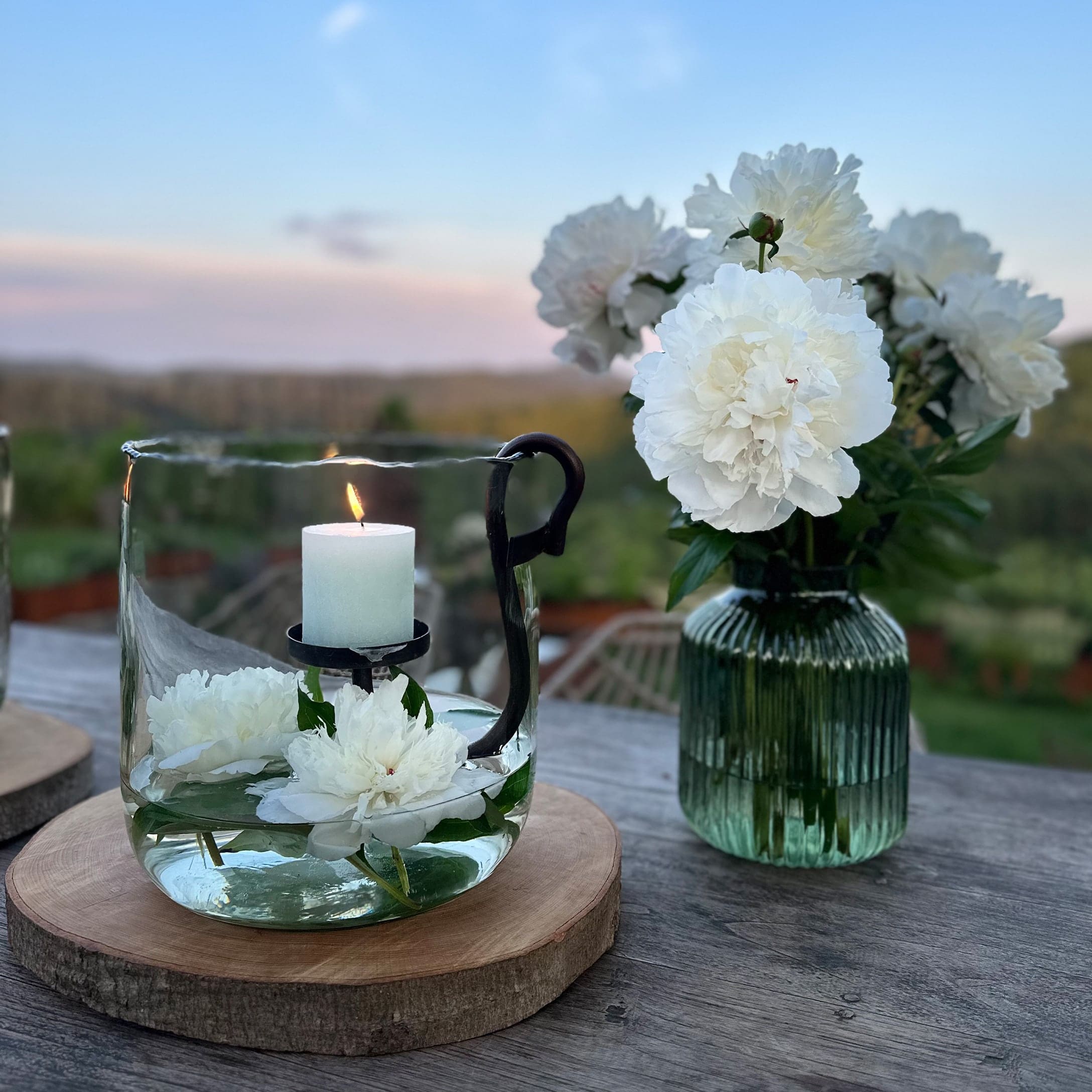 Bougeoir en verre avec bougie blanche et fleurs blanches sur base en bois en extérieur