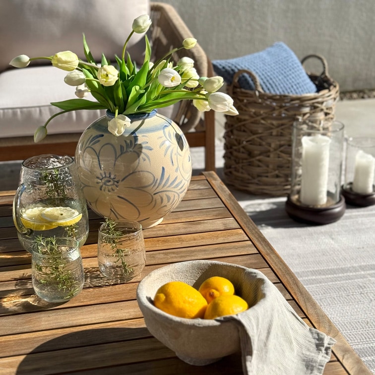 Vase en céramique décoratif avec motif floral et tulipes blanches sur table en bois en terrasse