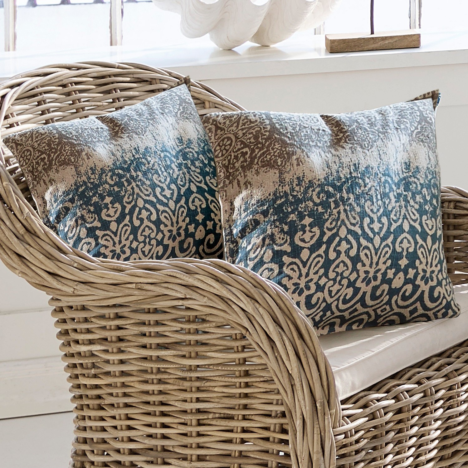 Coussin Rod Deux coussins décoratifs à motif bleu et beige sur un fauteuil en osier naturel