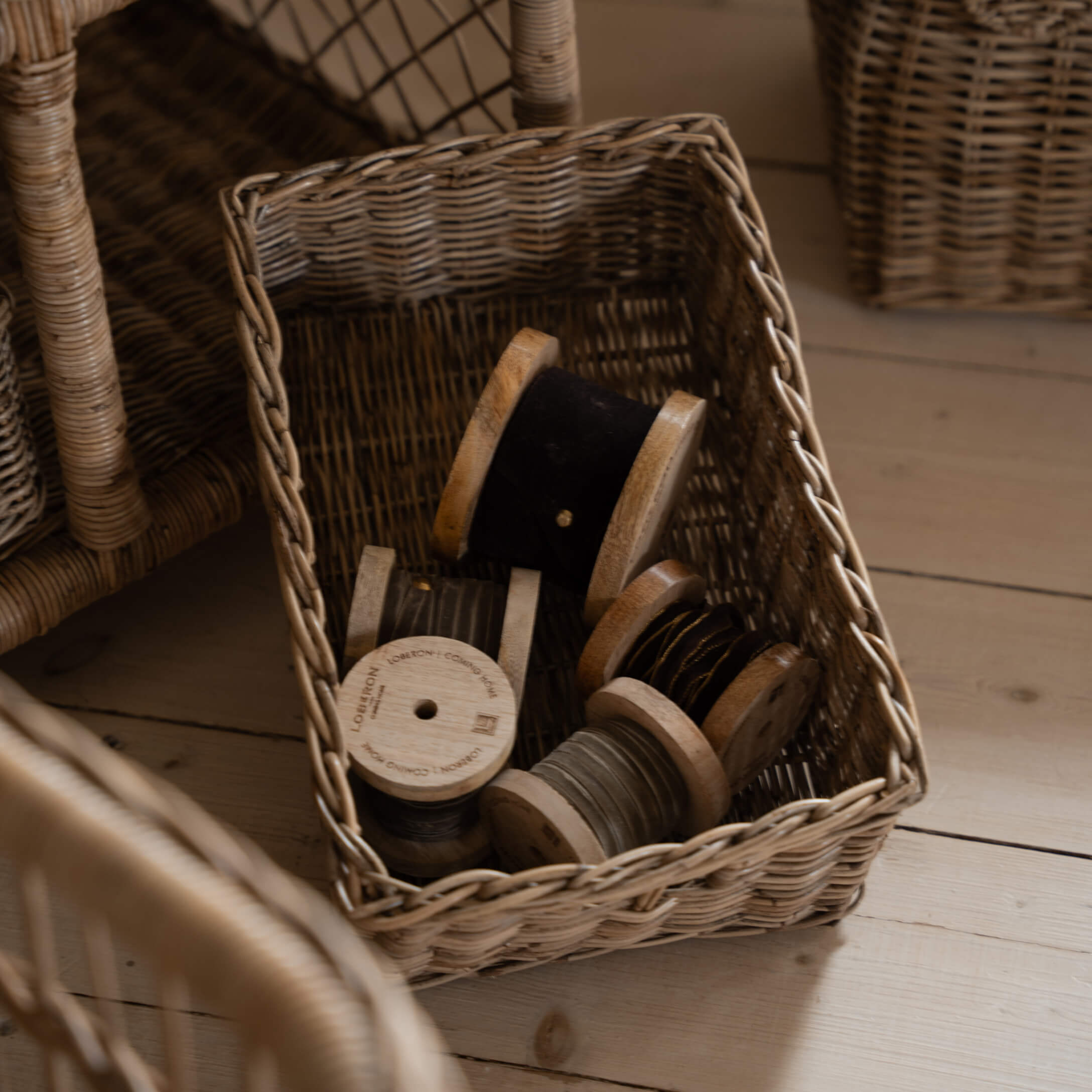 Panier en osier contenant des bobines en bois avec fils noirs et gris sur un sol en bois clair