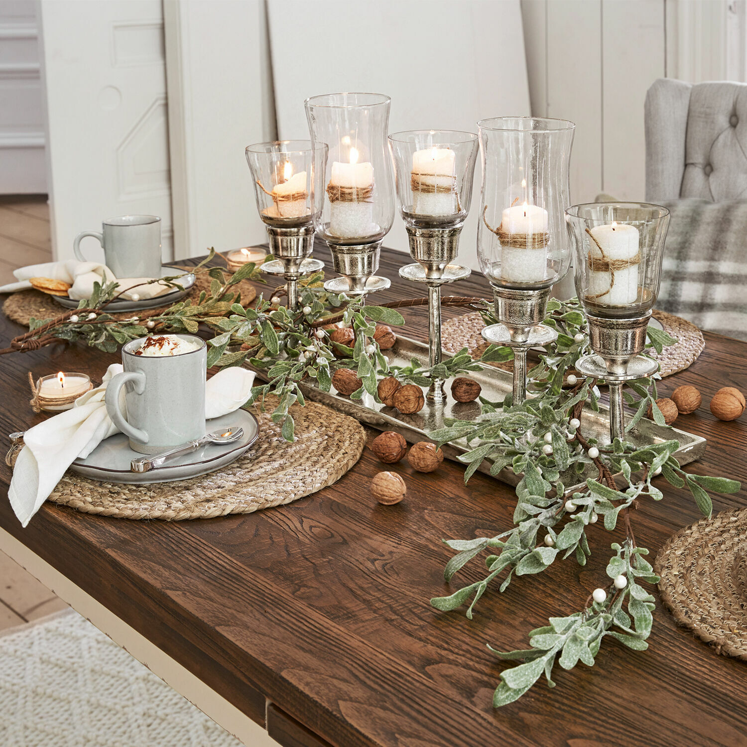Guirlande Cunnig Ensemble décoratif de bougeoirs en verre et métal sur table en bois avec branches vertes et noix