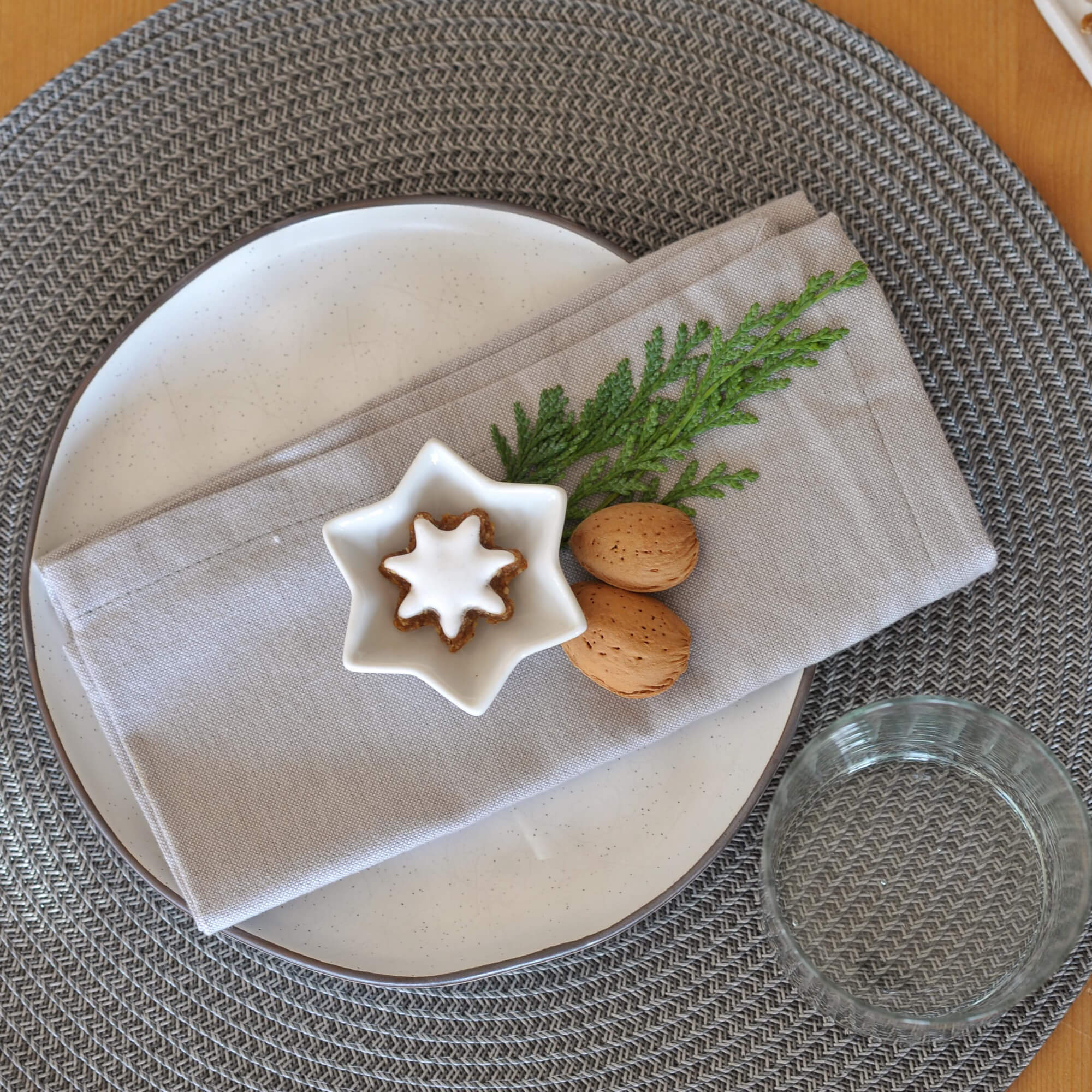 Set de table gris tressé avec assiette blanche, serviette en lin et décoration de Noël