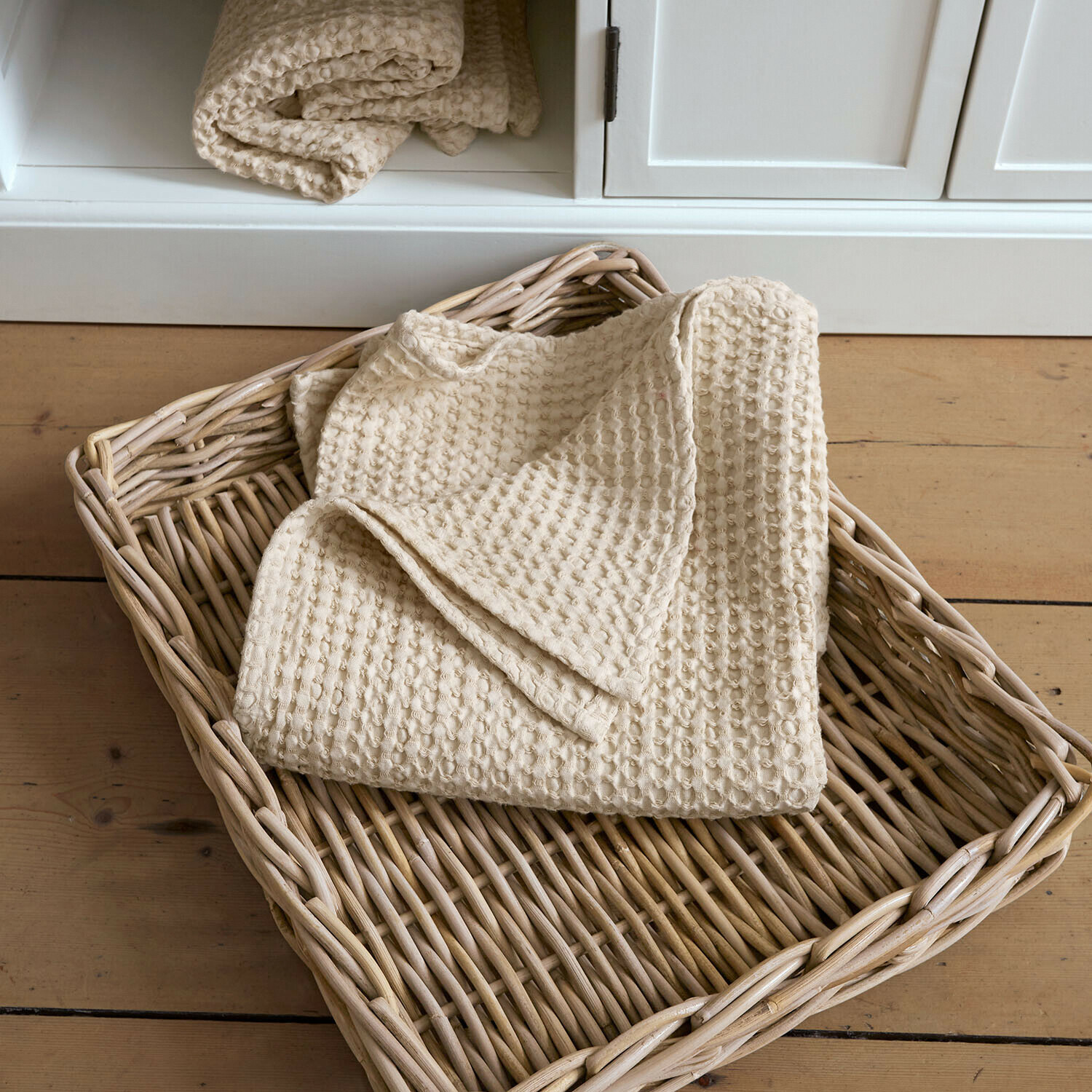 Serviette Maralei Plaid beige en coton gaufré dans un panier en osier posé sur un sol en bois clair