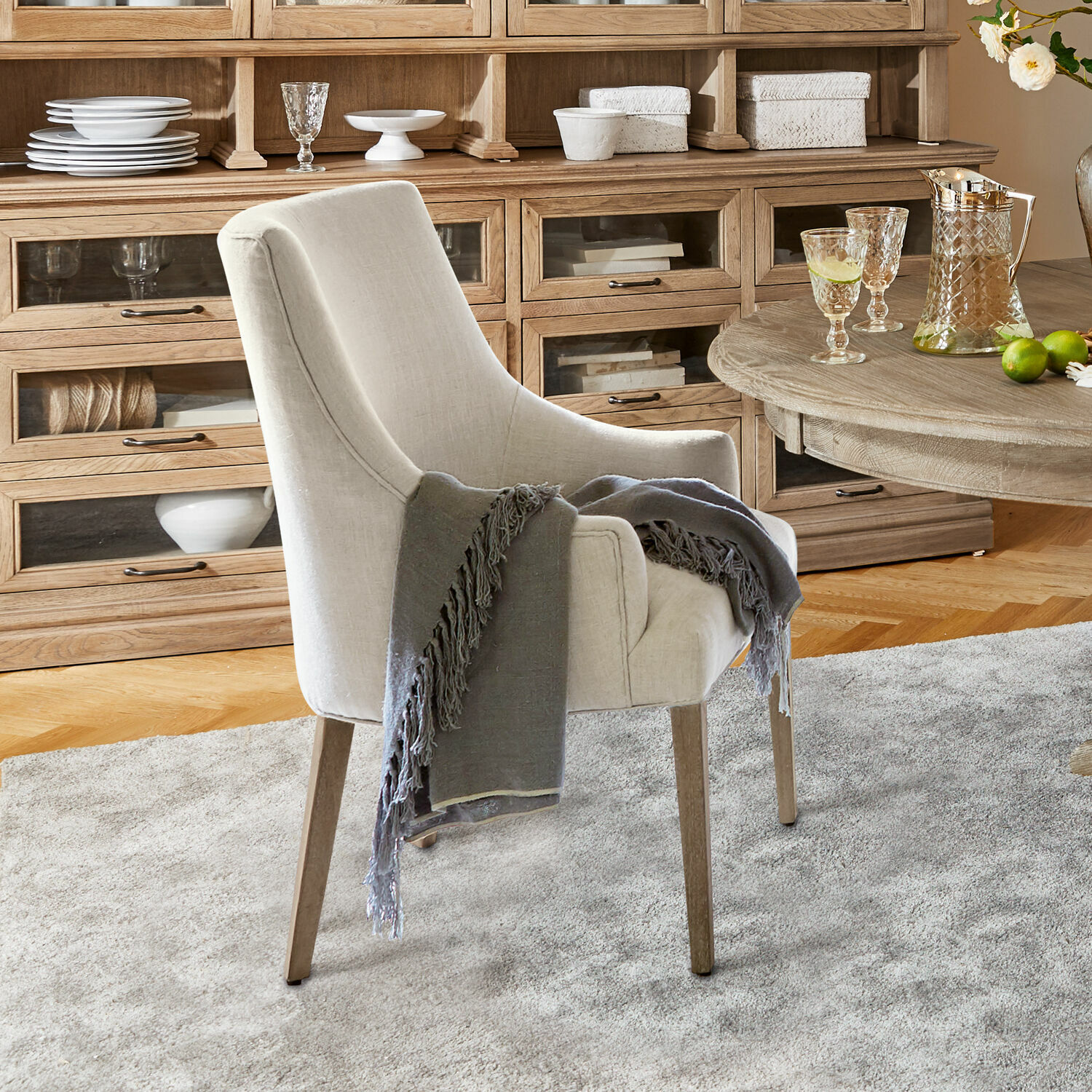Chaise Hyeres Fauteuil beige en tissu avec pieds en bois et plaid gris dans un salon chaleureux avec buffet en bois