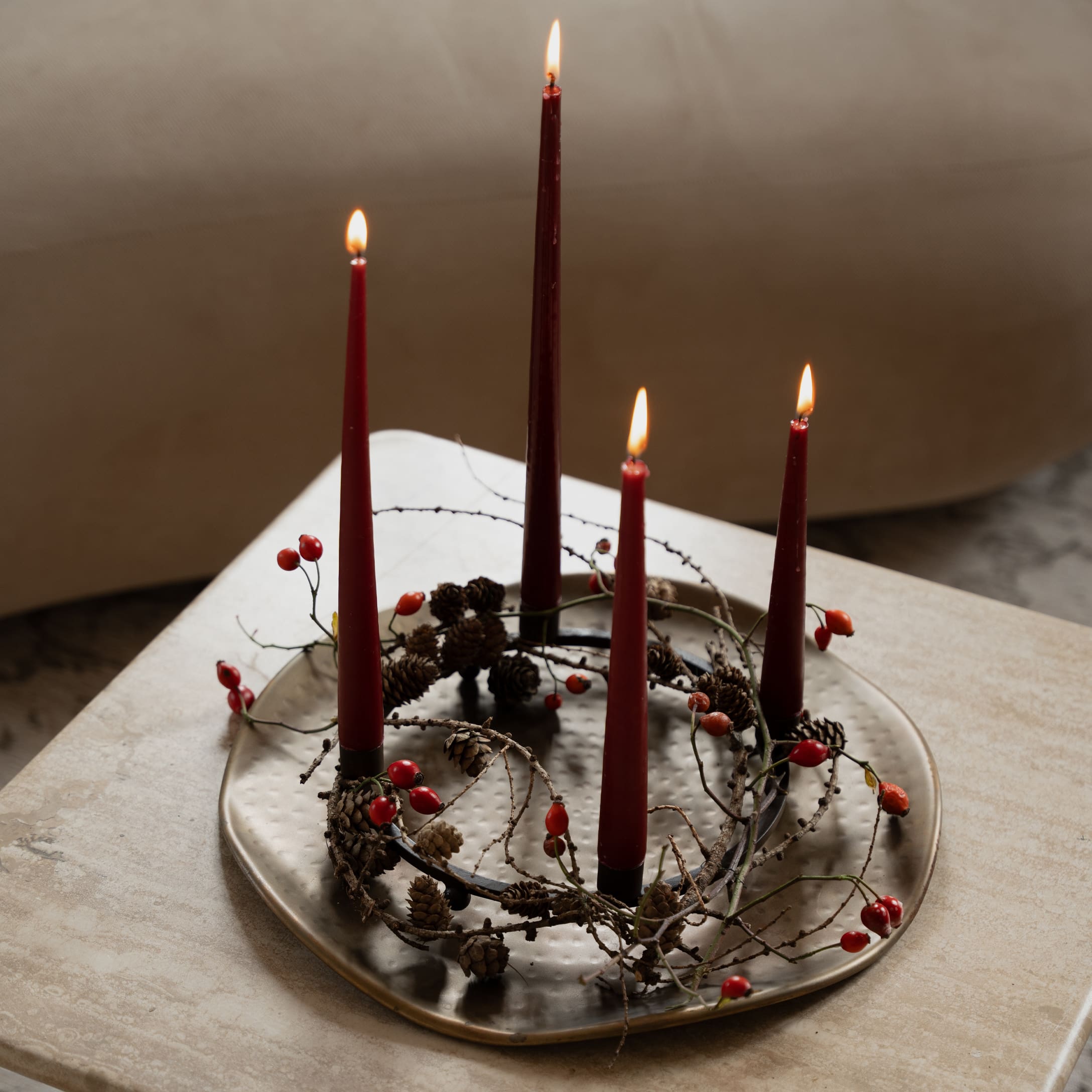 Couronne de l'Avent avec bougies rouges et pommes de pin sur plateau métallique posé sur une table claire