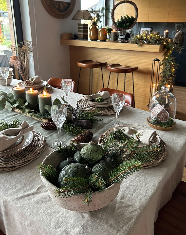 Table de fête décorée avec des branches vertes naturelles et des bougies dans un intérieur chaleureux