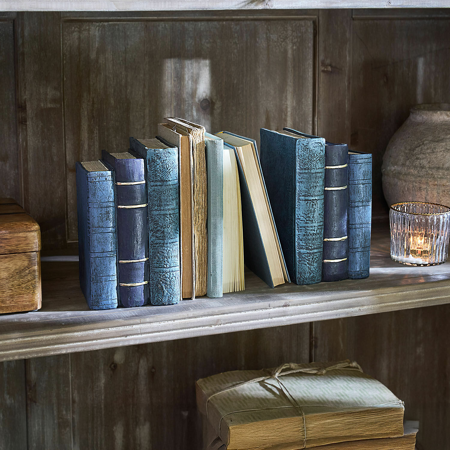 Lot de 2 serre-livres Morvini Collection de vieux livres aux couvertures bleues et beige sur une étagère en bois avec un photophore