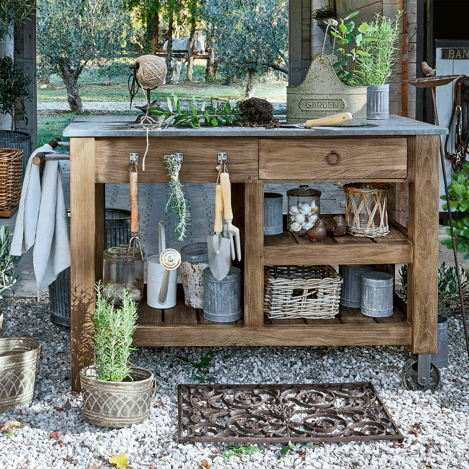 Table de rempotage Ellenton Table de jardin en bois avec outils de jardinage et pots sur sol en gravier dans un cadre naturel