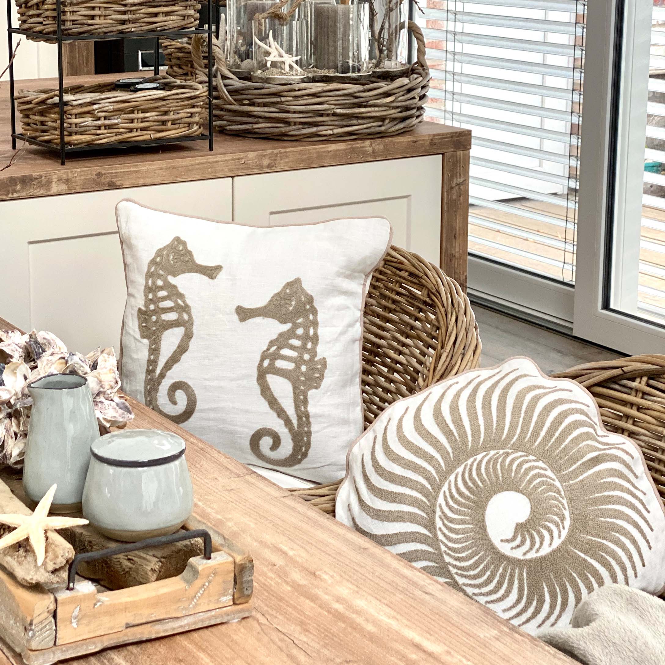 Coussins décoratifs avec motifs hippocampes et coquillages sur fauteuil en osier dans un intérieur lumineux