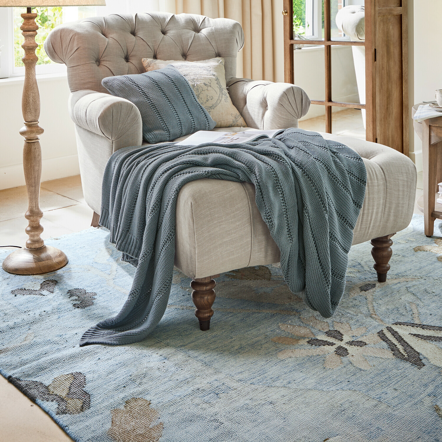 Plaid Lémeré Fauteuil beige en tissu avec dossier capitonné et plaid tricot bleu dans un salon lumineux