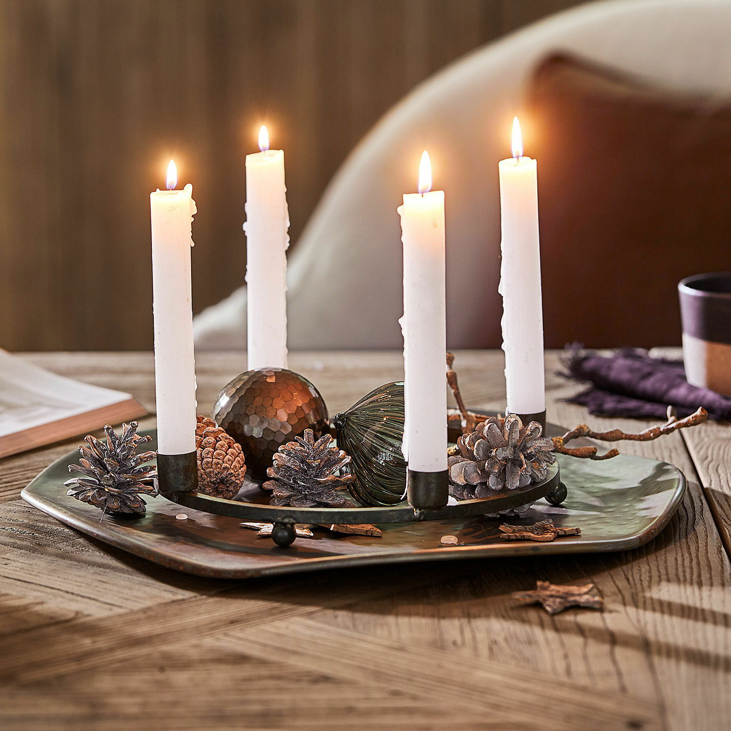 Couronne à bougies Nazeera Bougeoir en métal avec quatre bougies blanches et décorations de pommes de pin sur table en bois