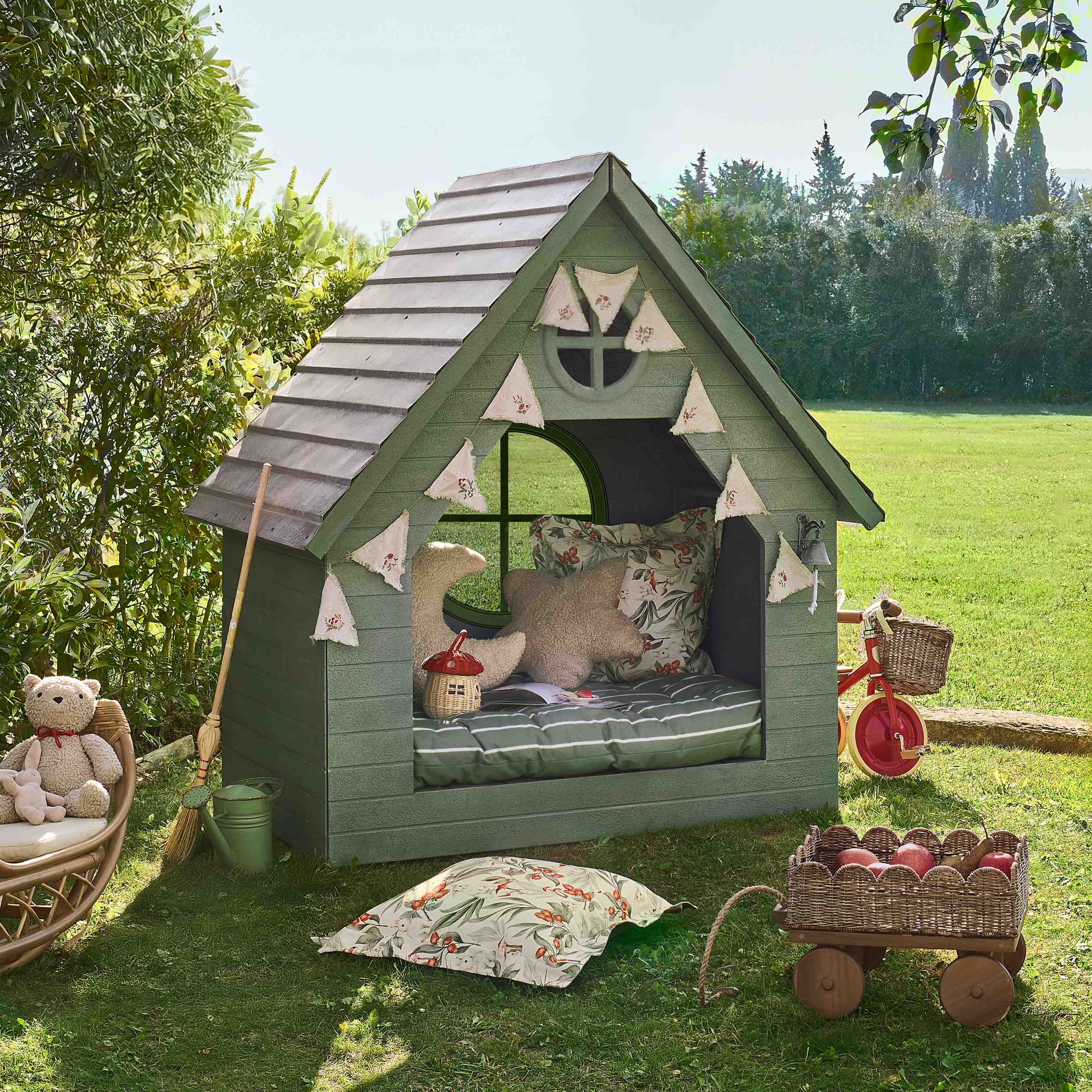 Maisonnette en bois verte pour enfants avec coussins et décorations dans un jardin sur l'herbe