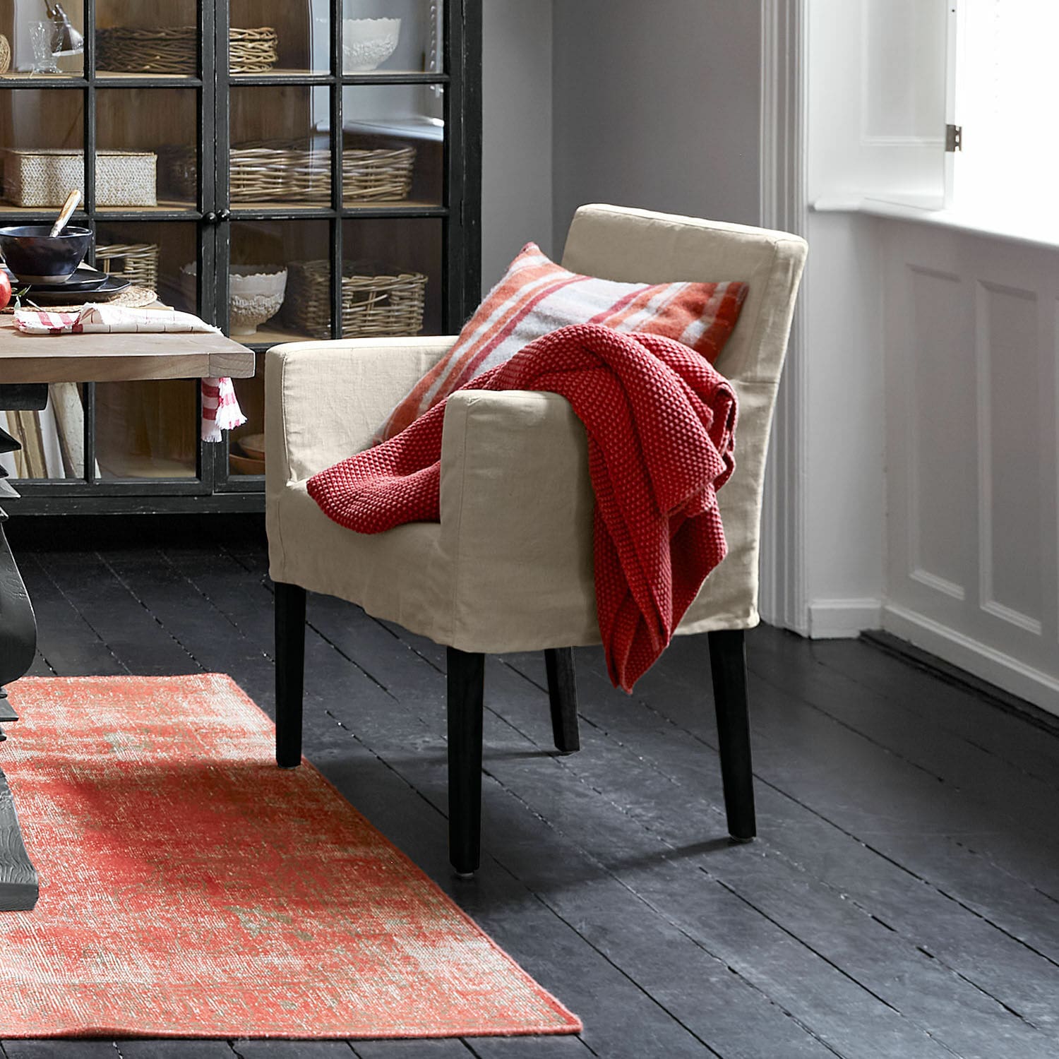 Chaise Longhill Fauteuil beige en tissu avec pieds noirs, plaid rouge et coussin à carreaux, tapis rouge à motifs