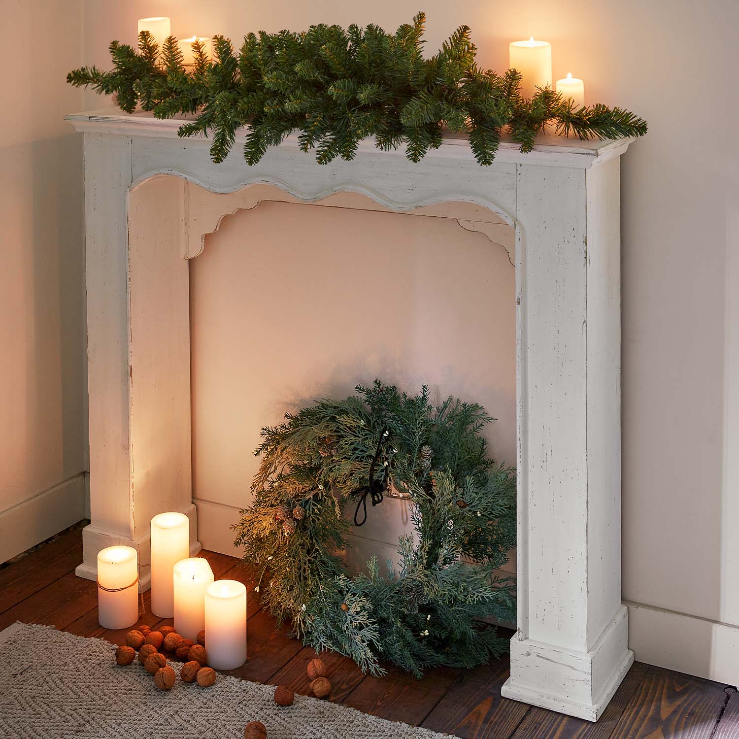Cheminée en bois blanc avec couronne verte et bougies allumées sur parquet, décoration de Noël chaleureuse