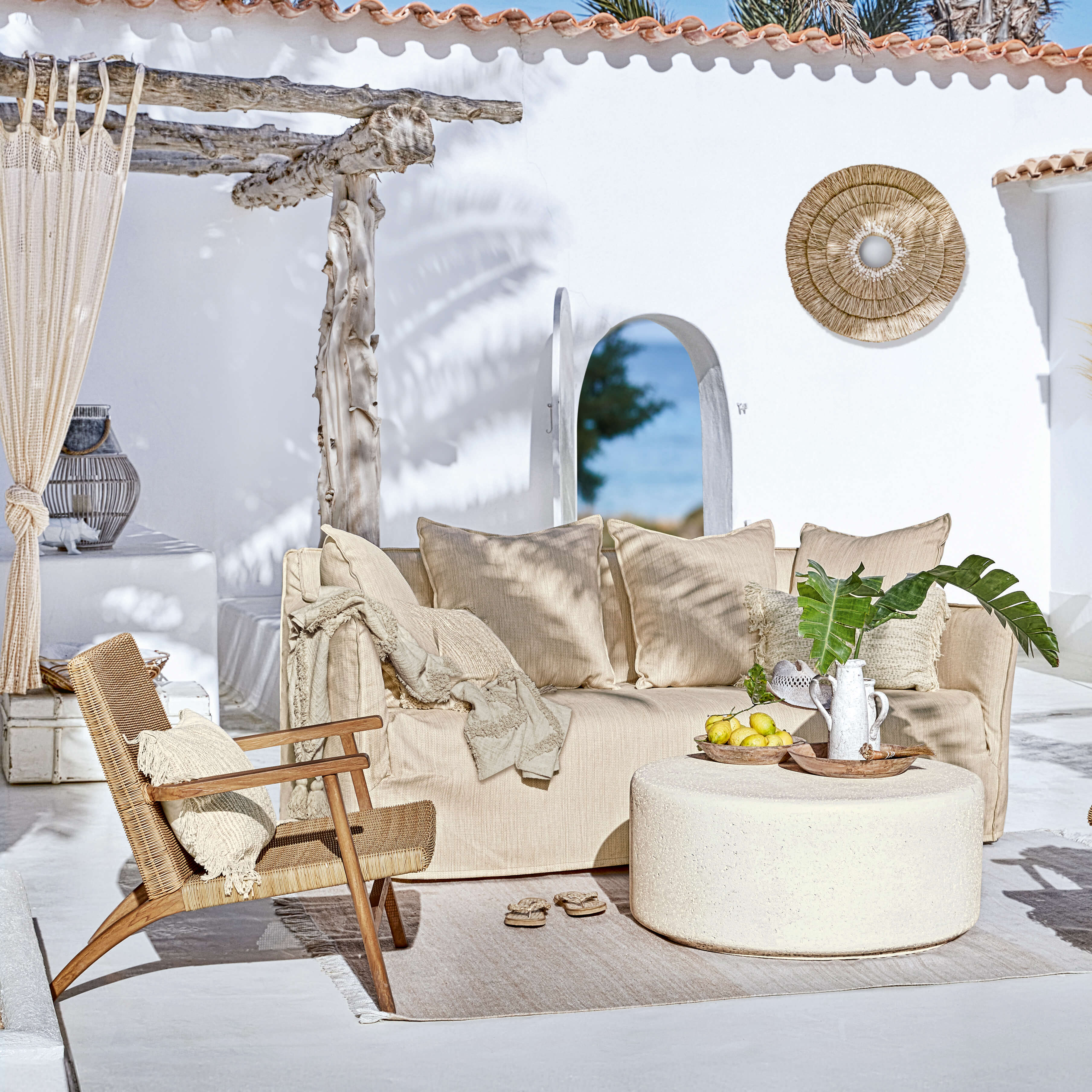 Canapé beige et fauteuil en rotin sur terrasse avec décorations naturelles et table basse ronde