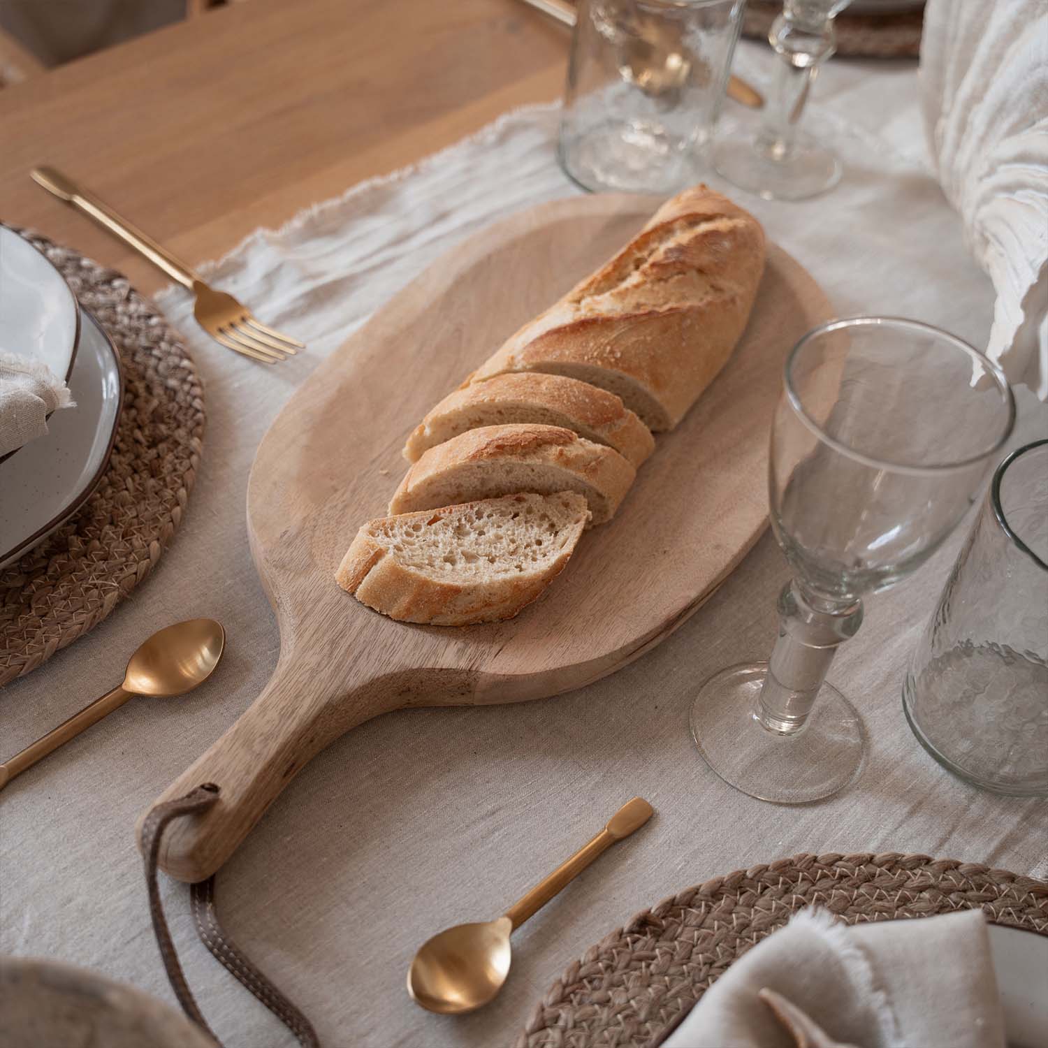 Planche à découper en bois avec baguette tranchée sur une table avec nappe naturelle et couverts dorés