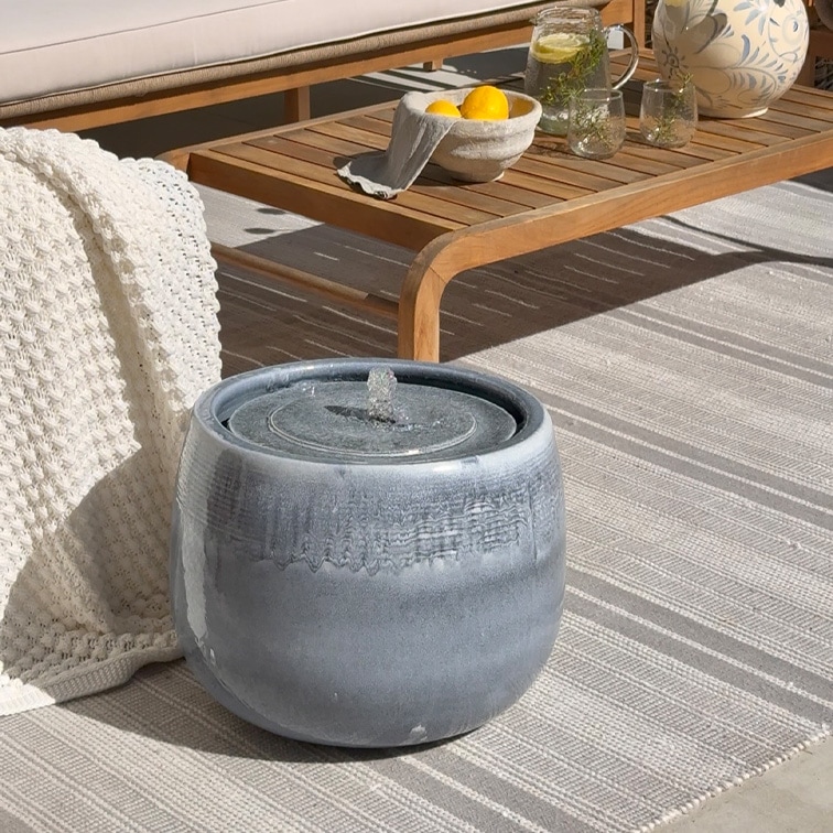 Fontaine de table en céramique grise sur tapis clair près d'une table en bois et d'une couverture blanche
