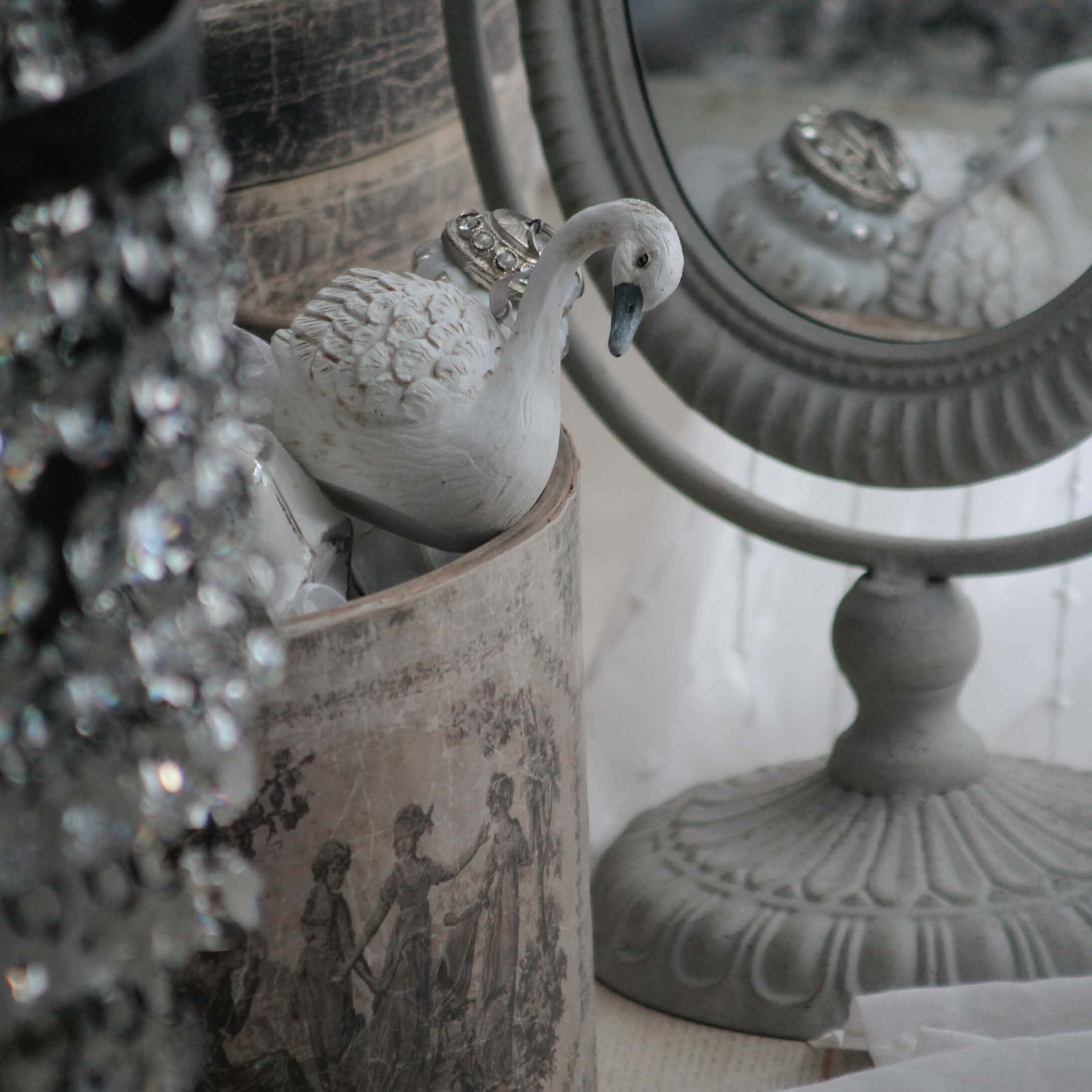 Figurine de cygne blanche en céramique près d'un miroir décoratif et d'un récipient vintage avec motif classique