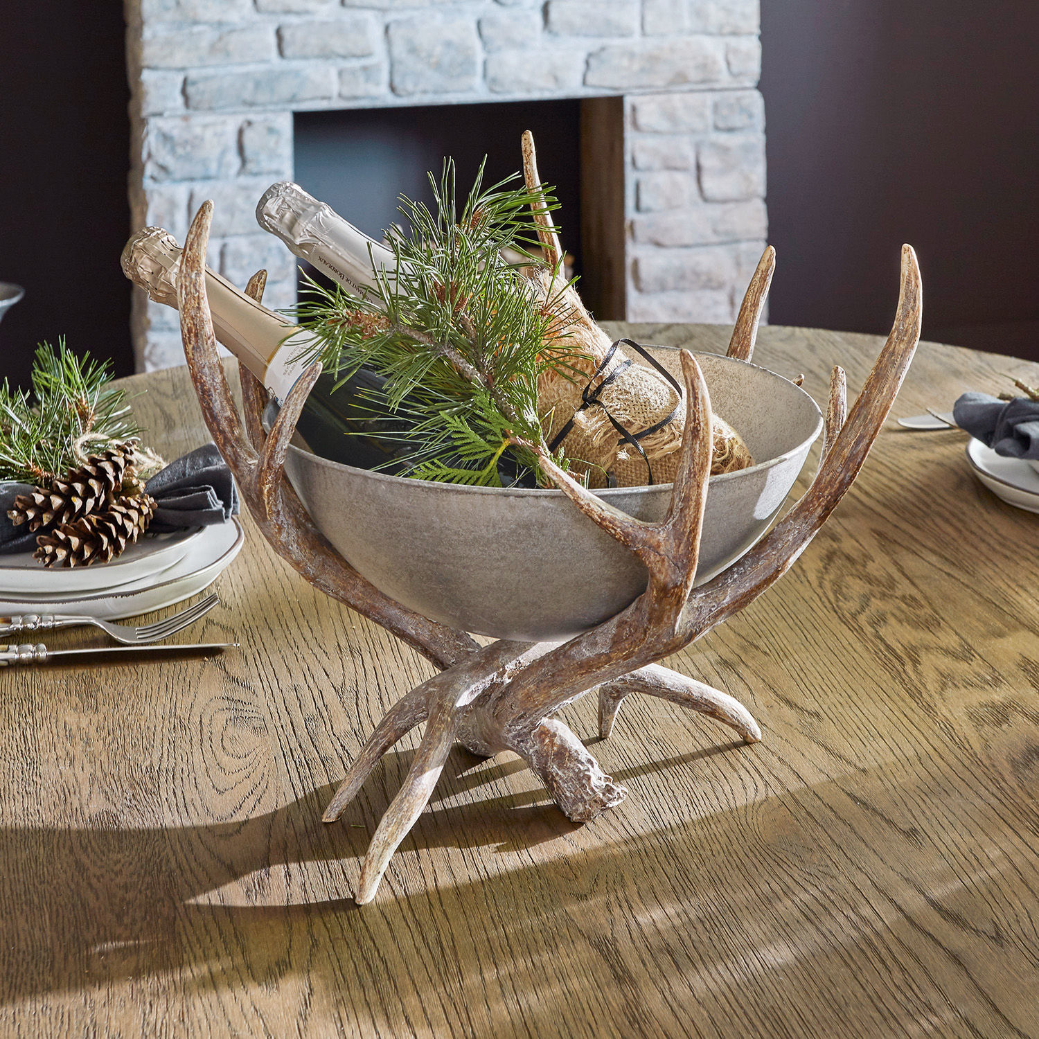 Coupe décorative Morlaix Bol en céramique grise sur support en bois de cerf avec bouteilles et branches vertes sur table en bois