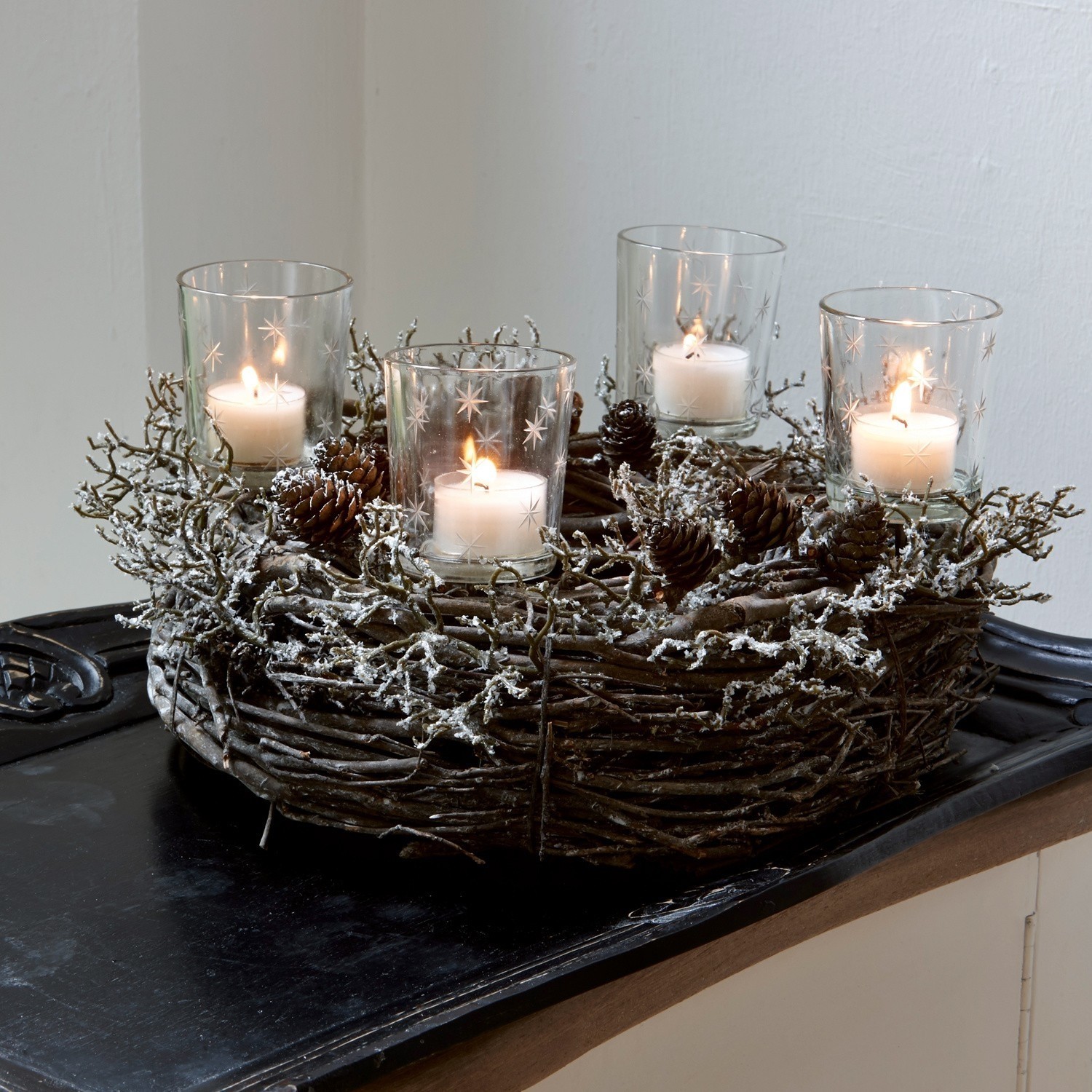 Lot de 4 photophores à planter Fenella Couronne décorative en branches et pommes de pin avec quatre bougies dans des photophores en verre sur un plateau noir