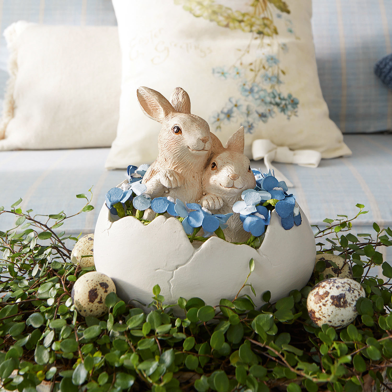 Lapins avec œuf Miksa Décoration avec deux lapins dans une coquille d'œuf blanche, fleurs bleues et feuillage vert