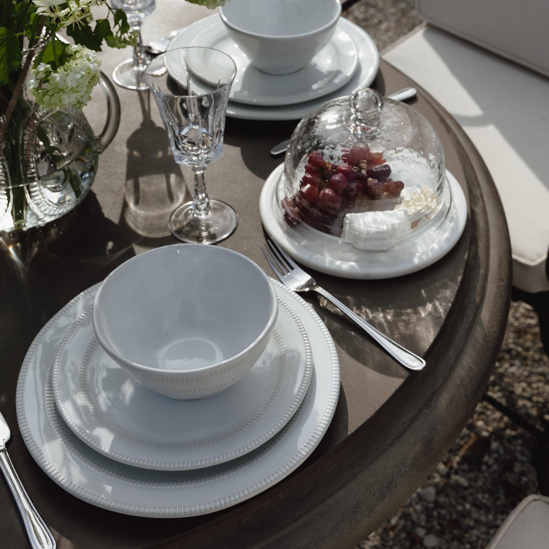 Service en porcelaine blanche sur table marron avec verre en cristal et cloche en verre contenant des raisins
