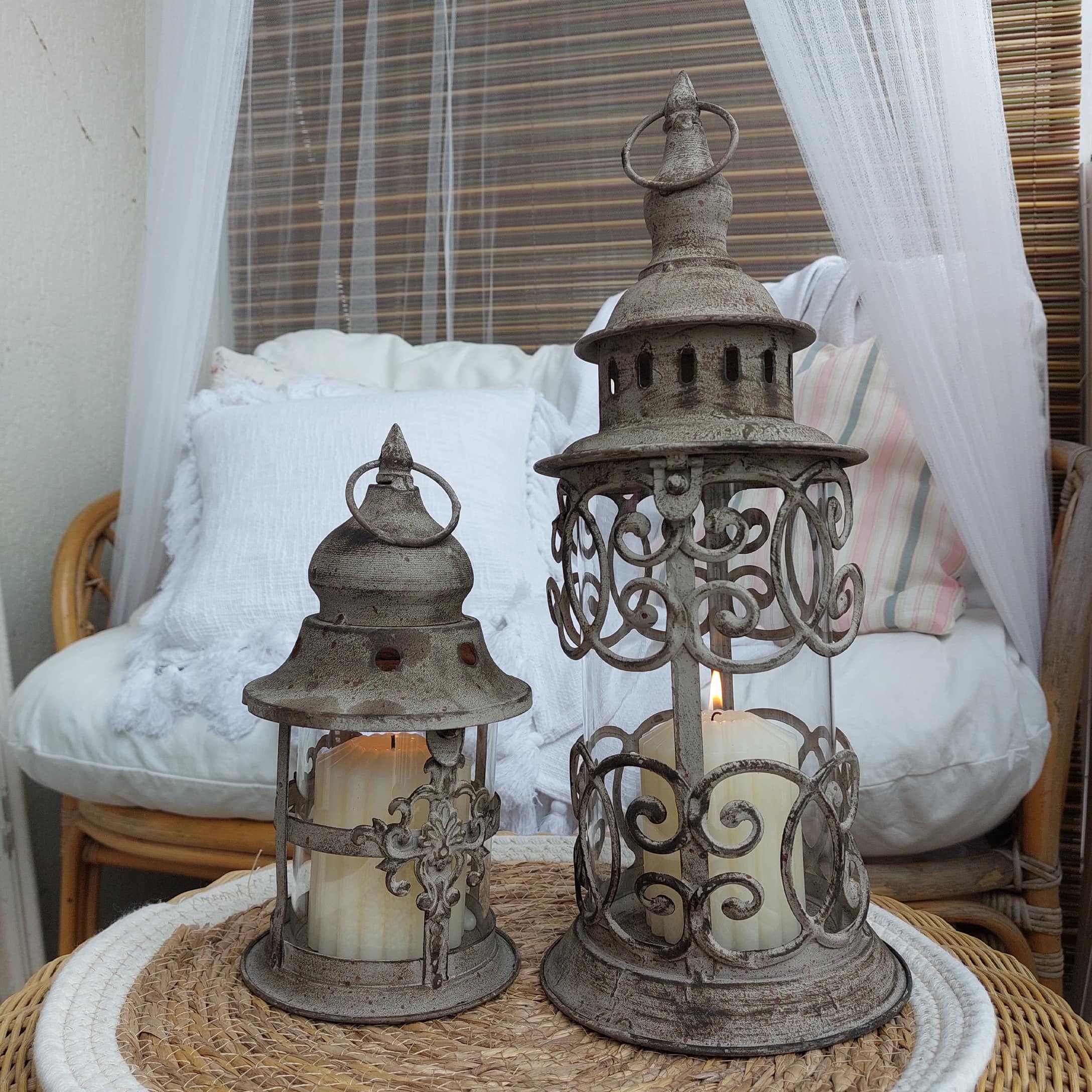 Deux lanternes décoratives en métal style vintage avec bougies blanches sur une table en osier