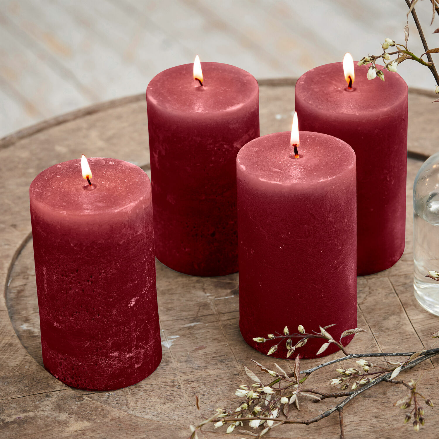 Lot de 4 bougies Braga Quatre bougies rouges en cire sur une table en bois avec décoration florale, ambiance chaleureuse