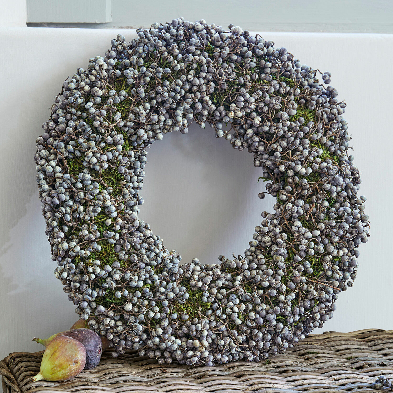 Couronne Elly Couronne décorative en baies séchées et mousse verte posée sur une table en osier, décoration saisonnière