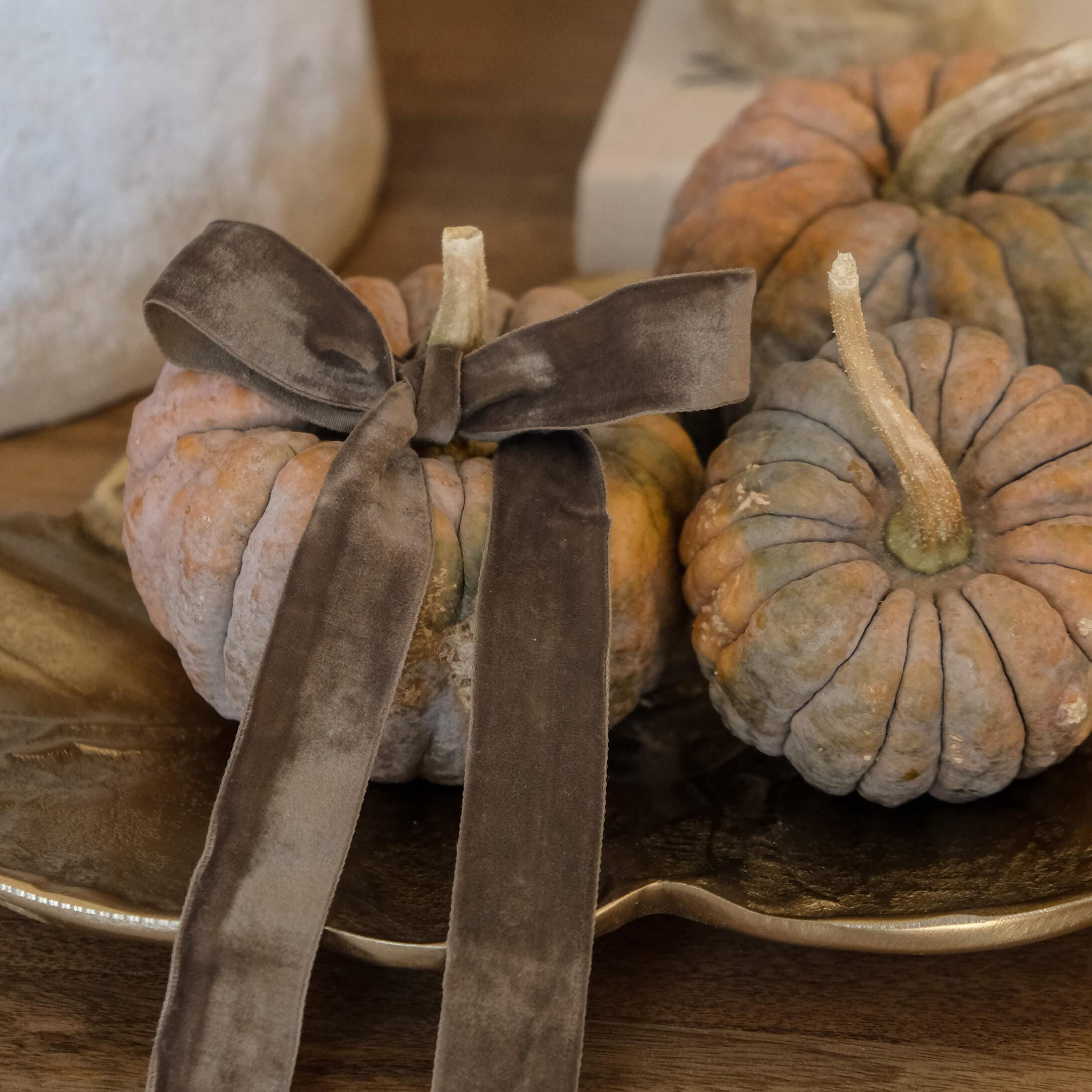 Citrouilles décoratives orange-gris avec un nœud en velours marron sur un plateau doré en bois