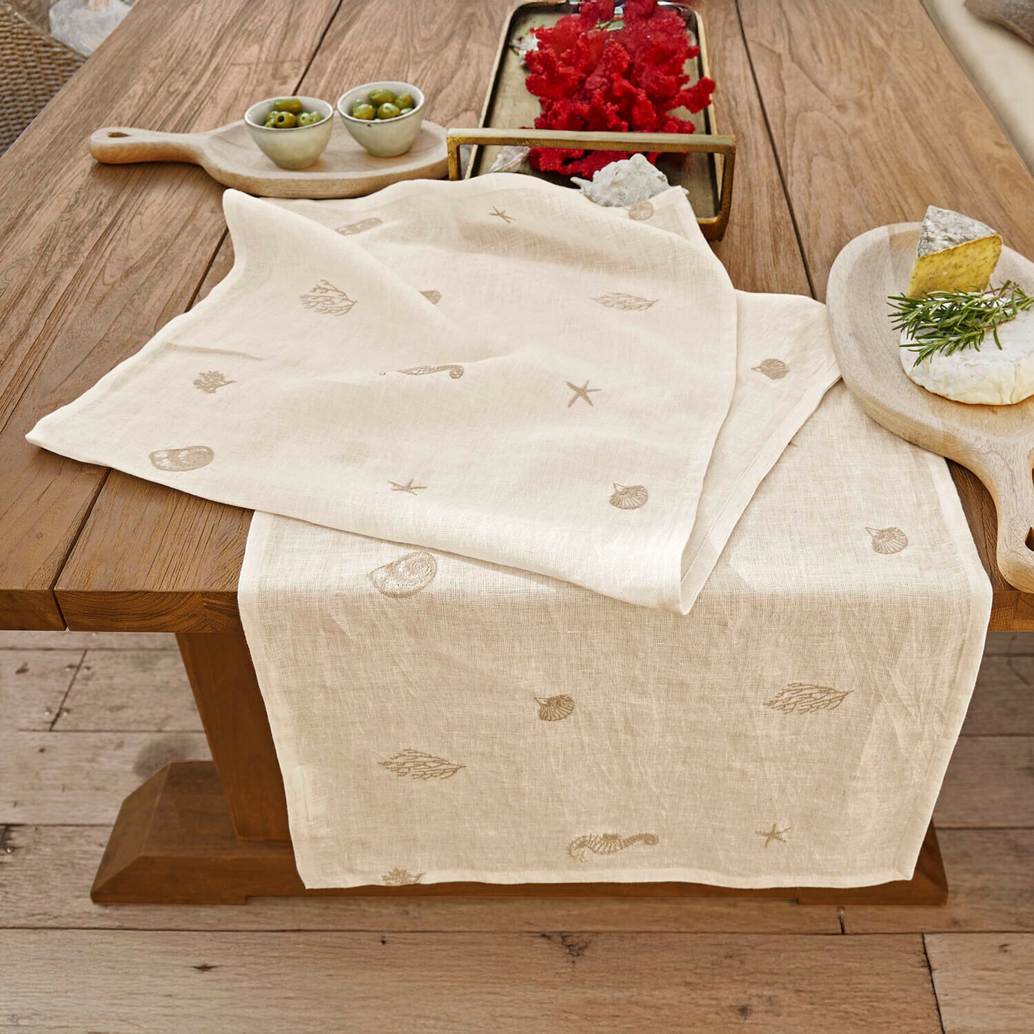 Chemin de table Celorin Chemin de table en lin beige avec motifs marins brodés sur une table en bois pour décoration intérieure