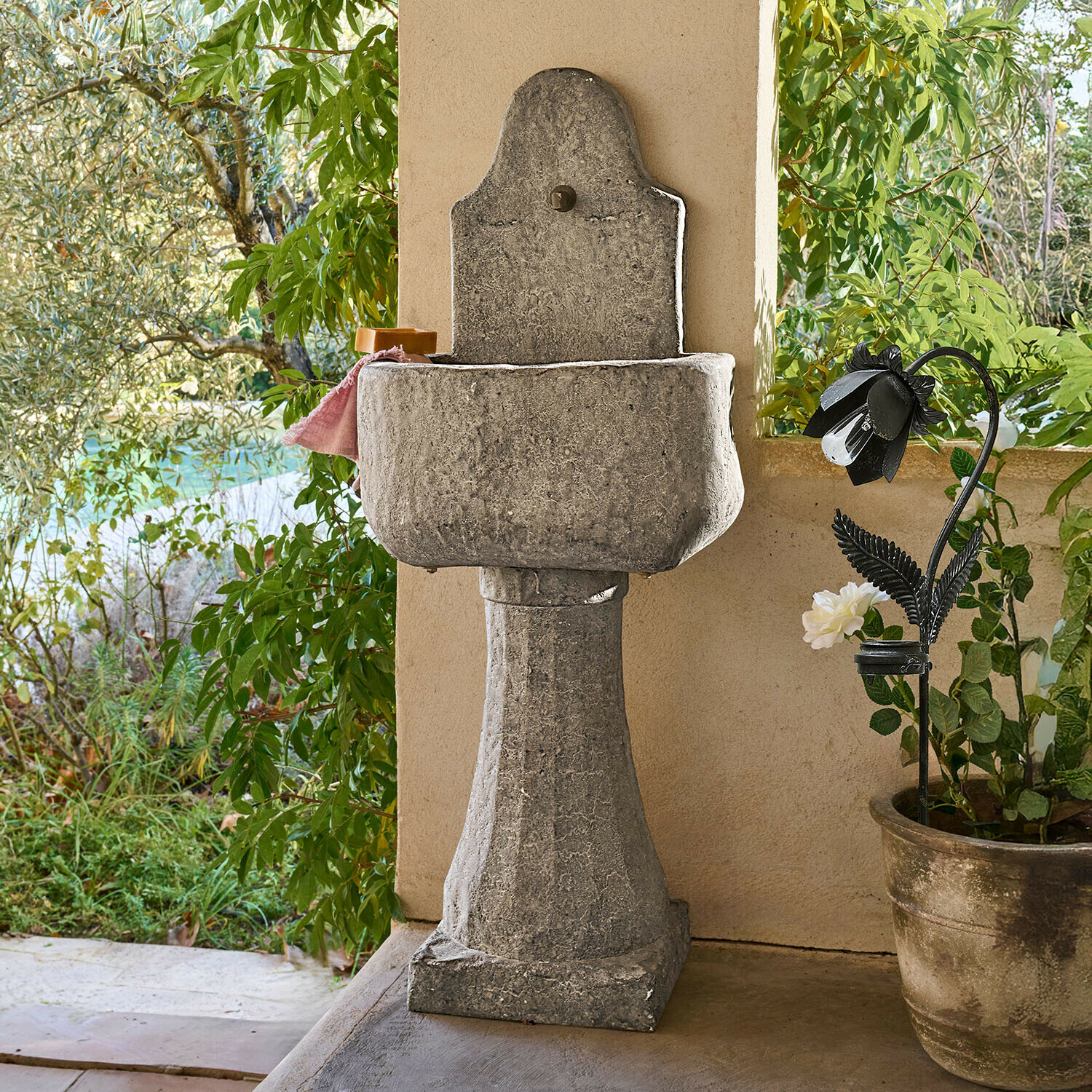 Lavabo de jardin en pierre grise sur colonne avec finition naturelle, entouré de plantes vertes