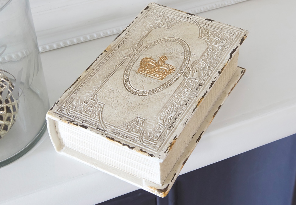 Livre décoratif shabby chic avec couverture blanche vieillie et couronne dorée sur une étagère