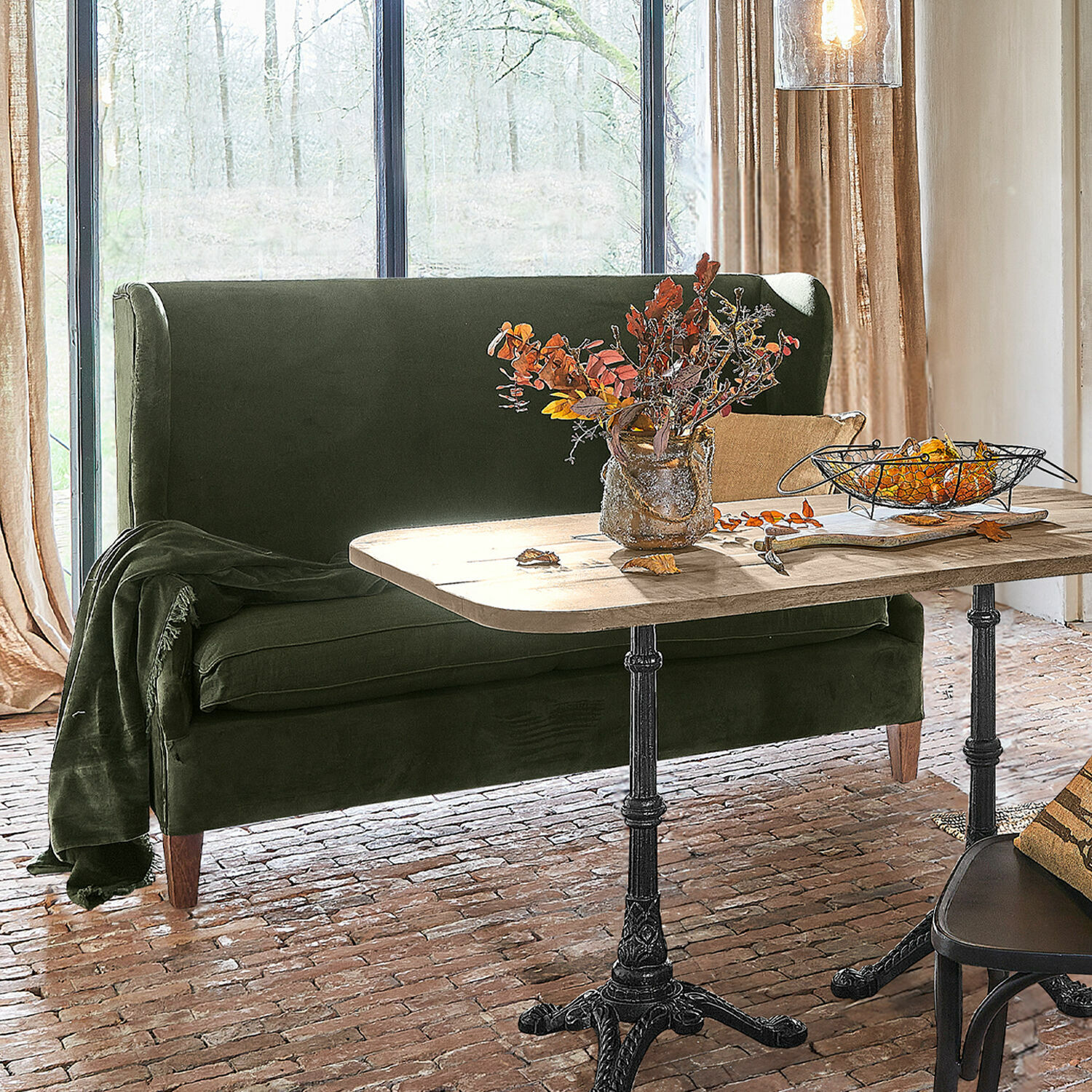 Canapé Ombra Canapé vert en velours près d'une table en bois avec pieds en métal dans un salon lumineux au sol en briques
