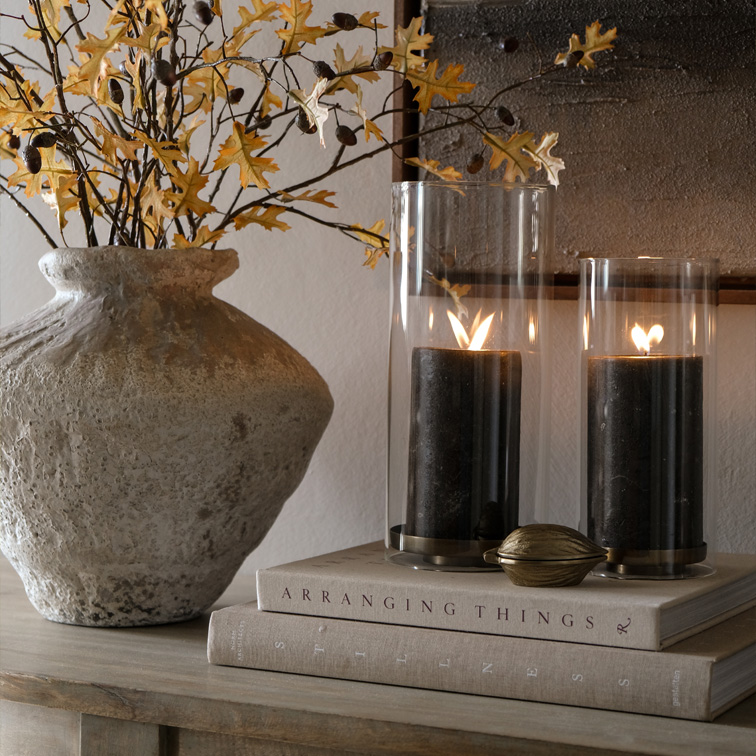 Vase en pierre décoratif avec branches sèches et deux bougies noires dans des photophores en verre sur des livres