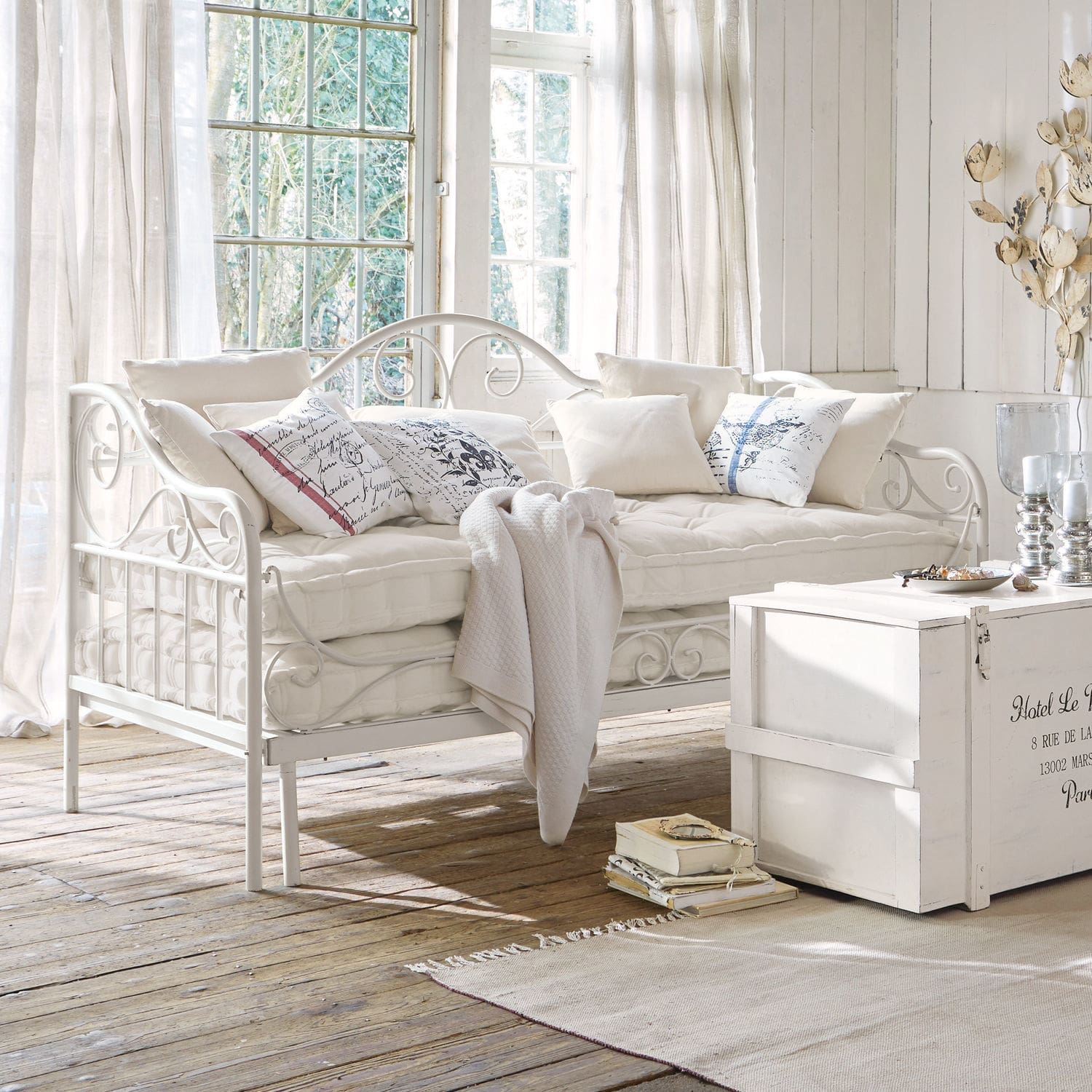 Banquette Maditha Canapé en métal blanc avec coussins doux et plaid dans un intérieur lumineux au sol en bois naturel