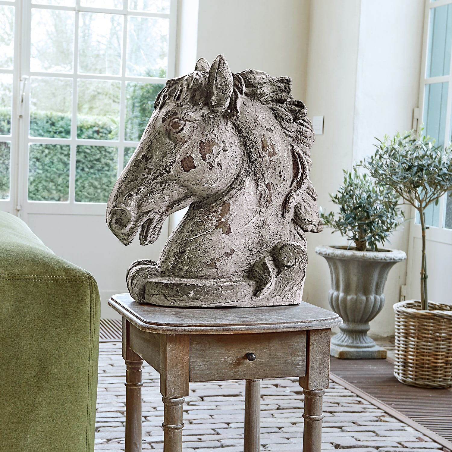 Sculpture tête de cheval en béton vieilli gris posée sur une table en bois dans un intérieur lumineux