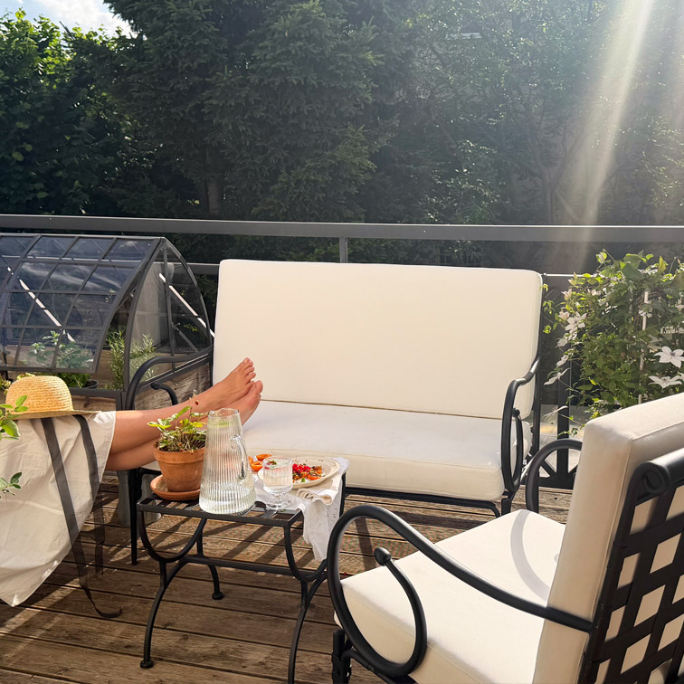 Ensemble de mobilier de jardin blanc avec cadre en métal et coussins sur terrasse en bois avec plantes et carafe en verre