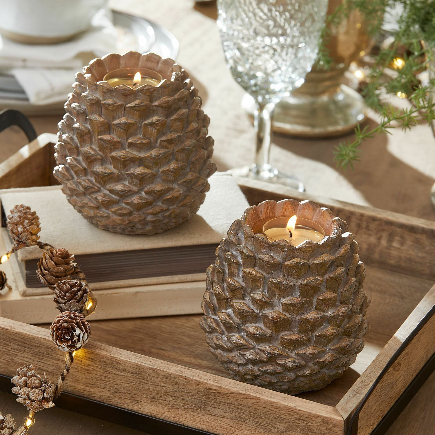 Lot de 2 photophores Butz Deux bougeoirs en résine marron en forme de pommes de pin sur un plateau en bois, décoration de table